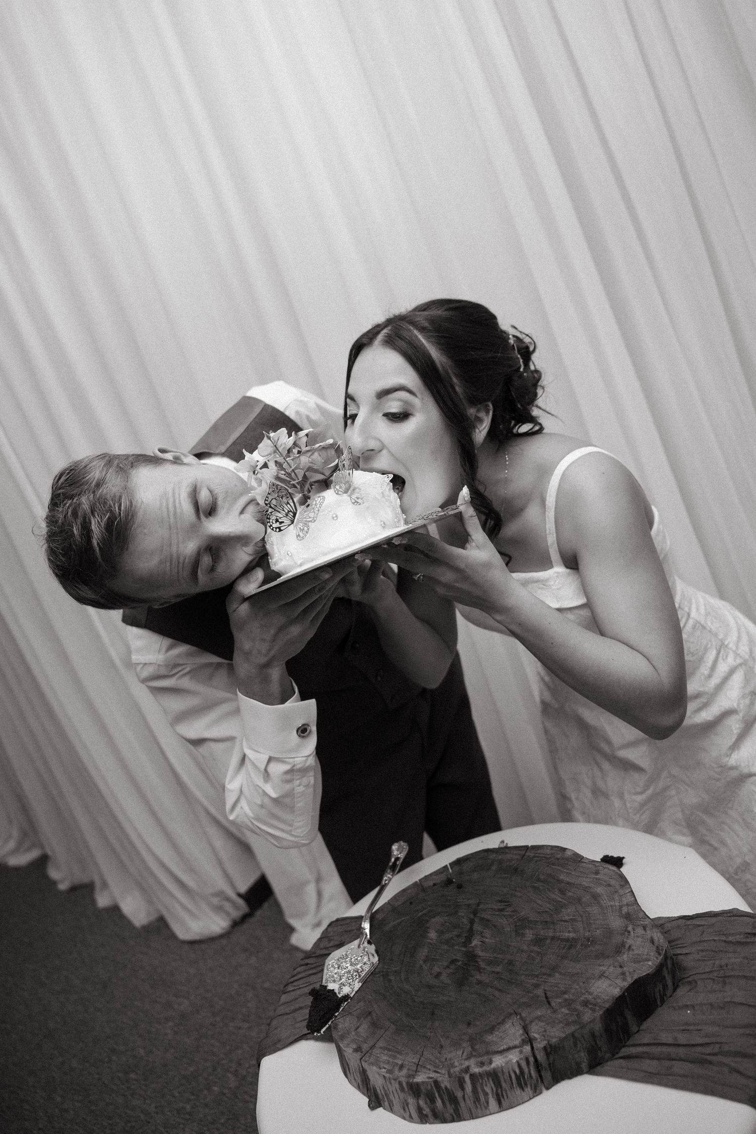 Black and white photo of bride and groom eating wedding cake together at reception in the Drakensberg.