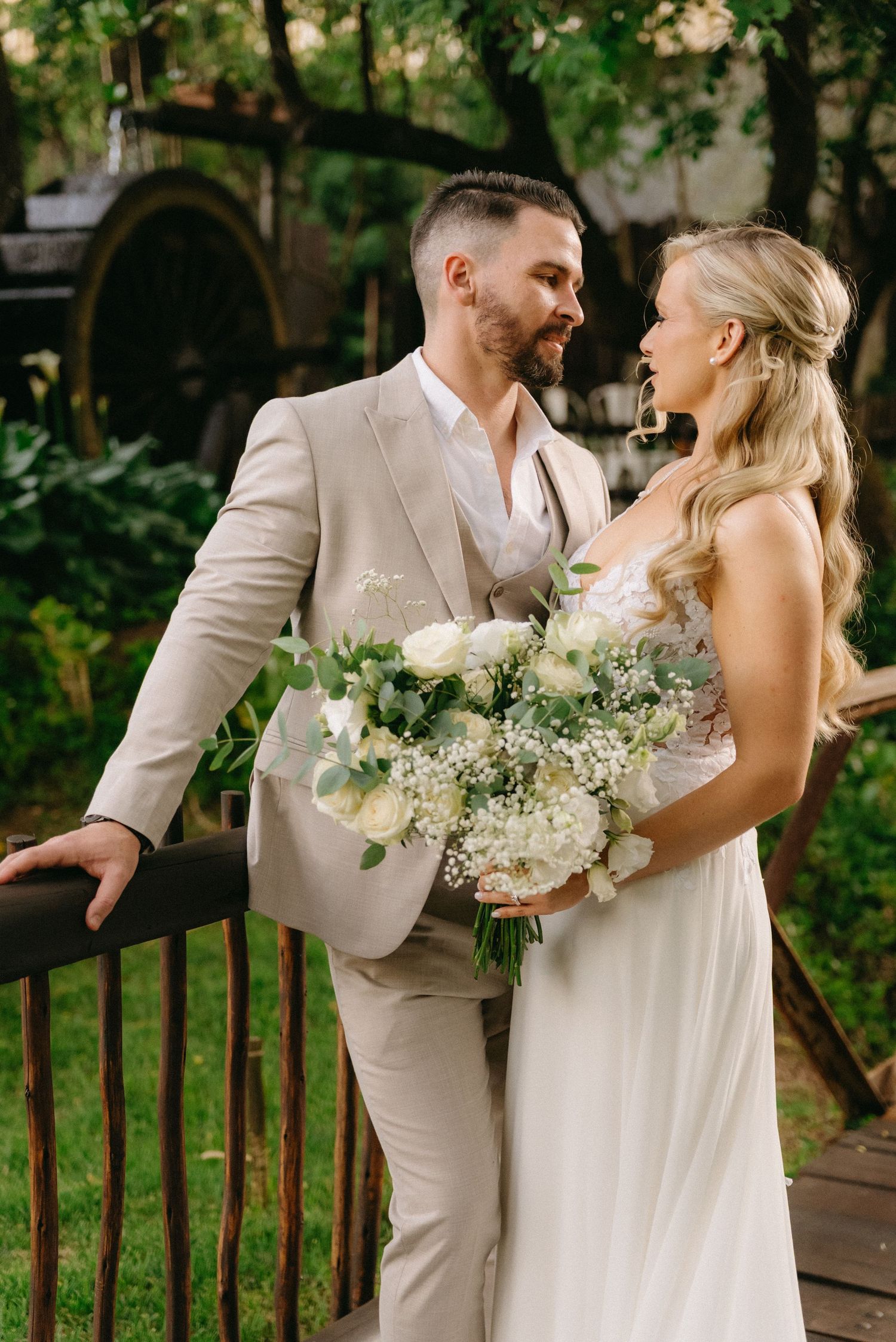 Couple shares intimate moment on wooden deck with white floral bouquet.