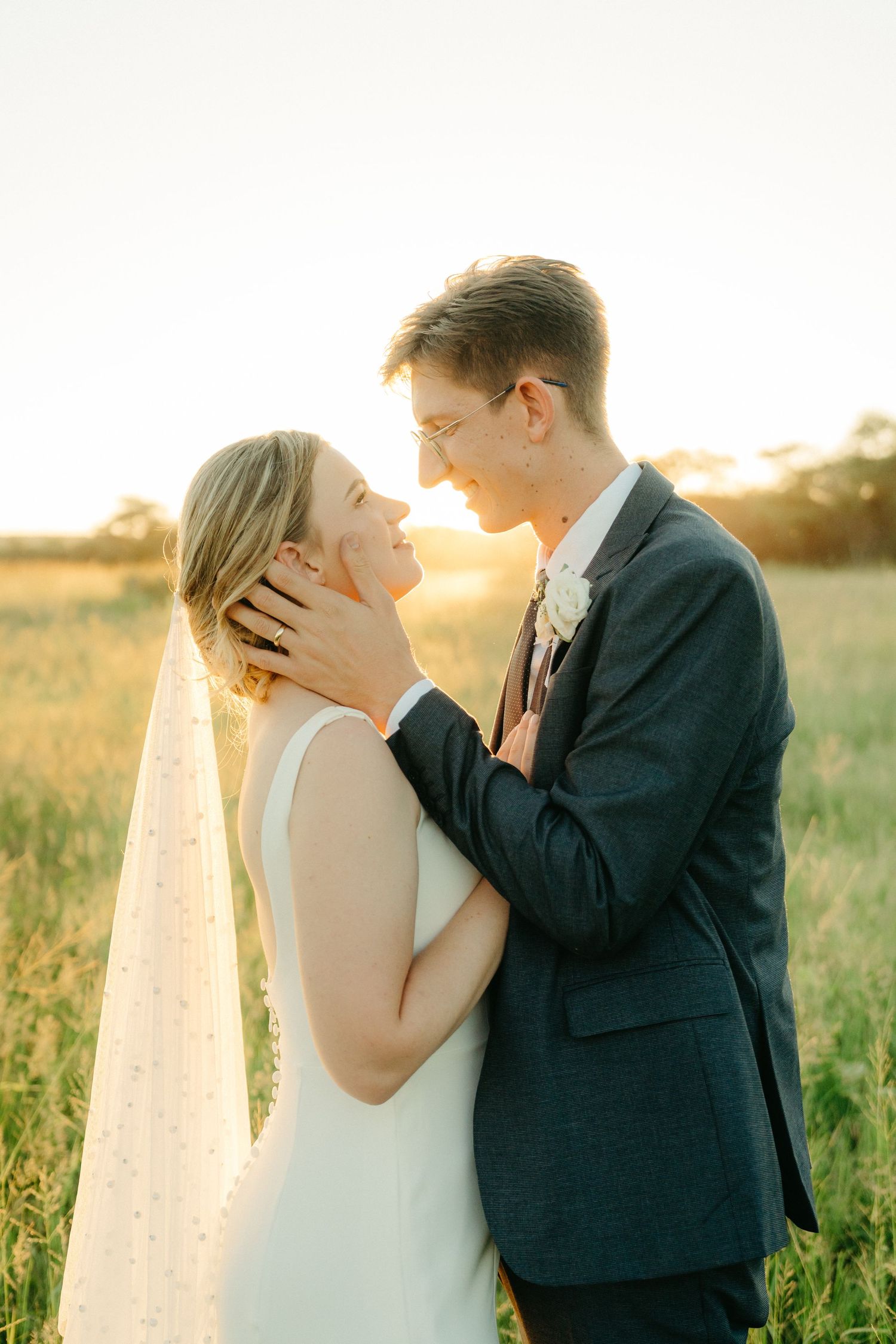 A bride and groom share an intimate moment in a golden sunset field during their wedding photoshoot.