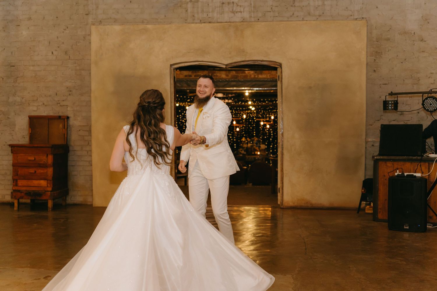 Bride and groom share first dance in elegant industrial venue with warm lighting.