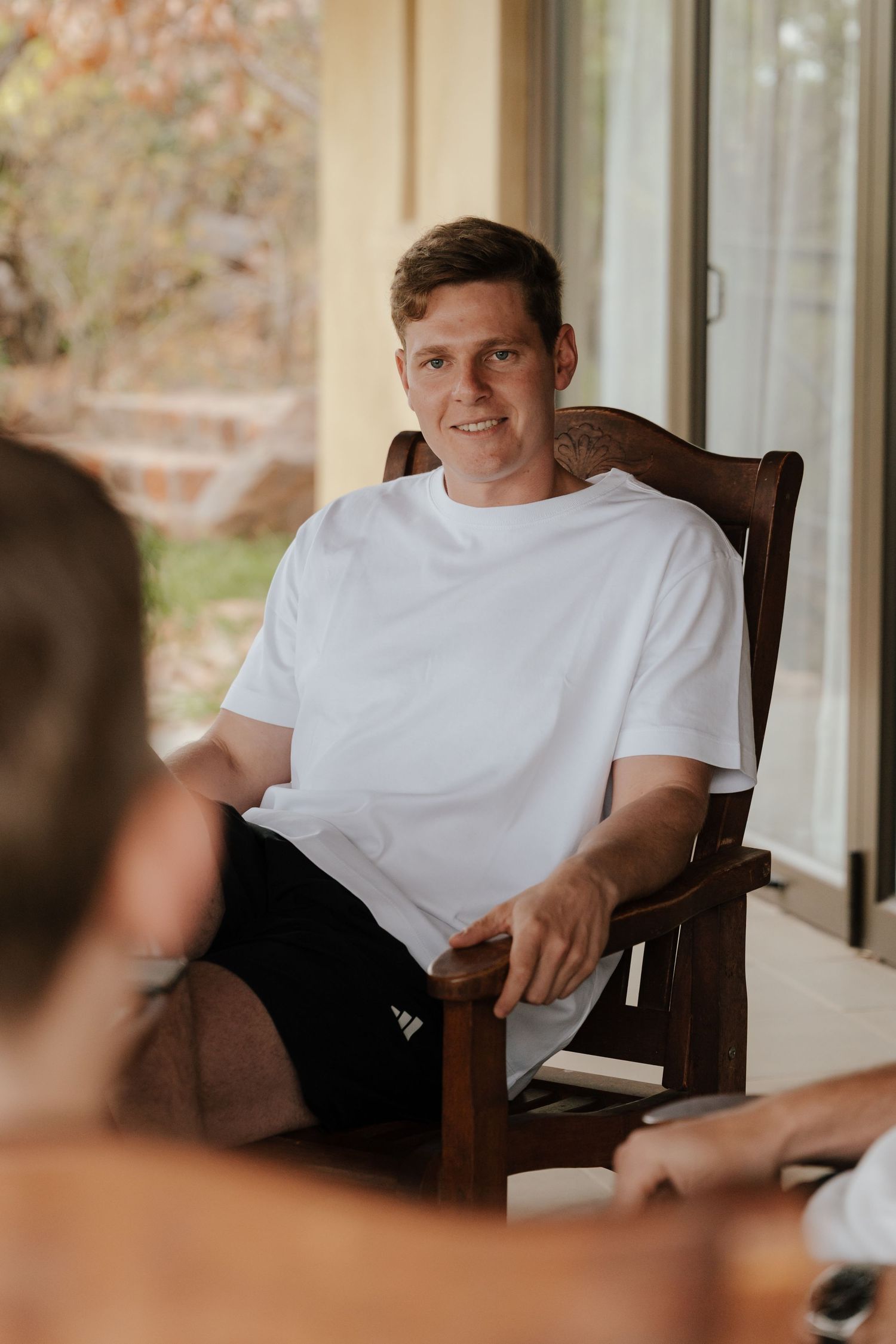 Wedding guest relaxing in wooden chair by window.