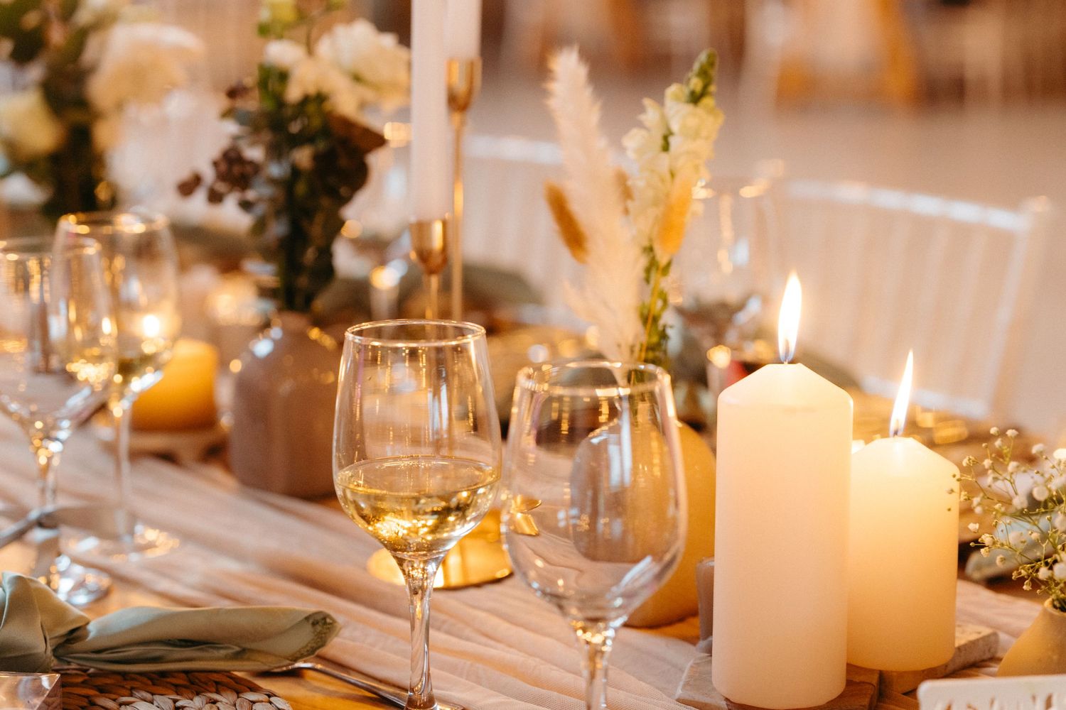 An elegant wedding table setting with lit candles, wine glasses and dried floral arrangements.