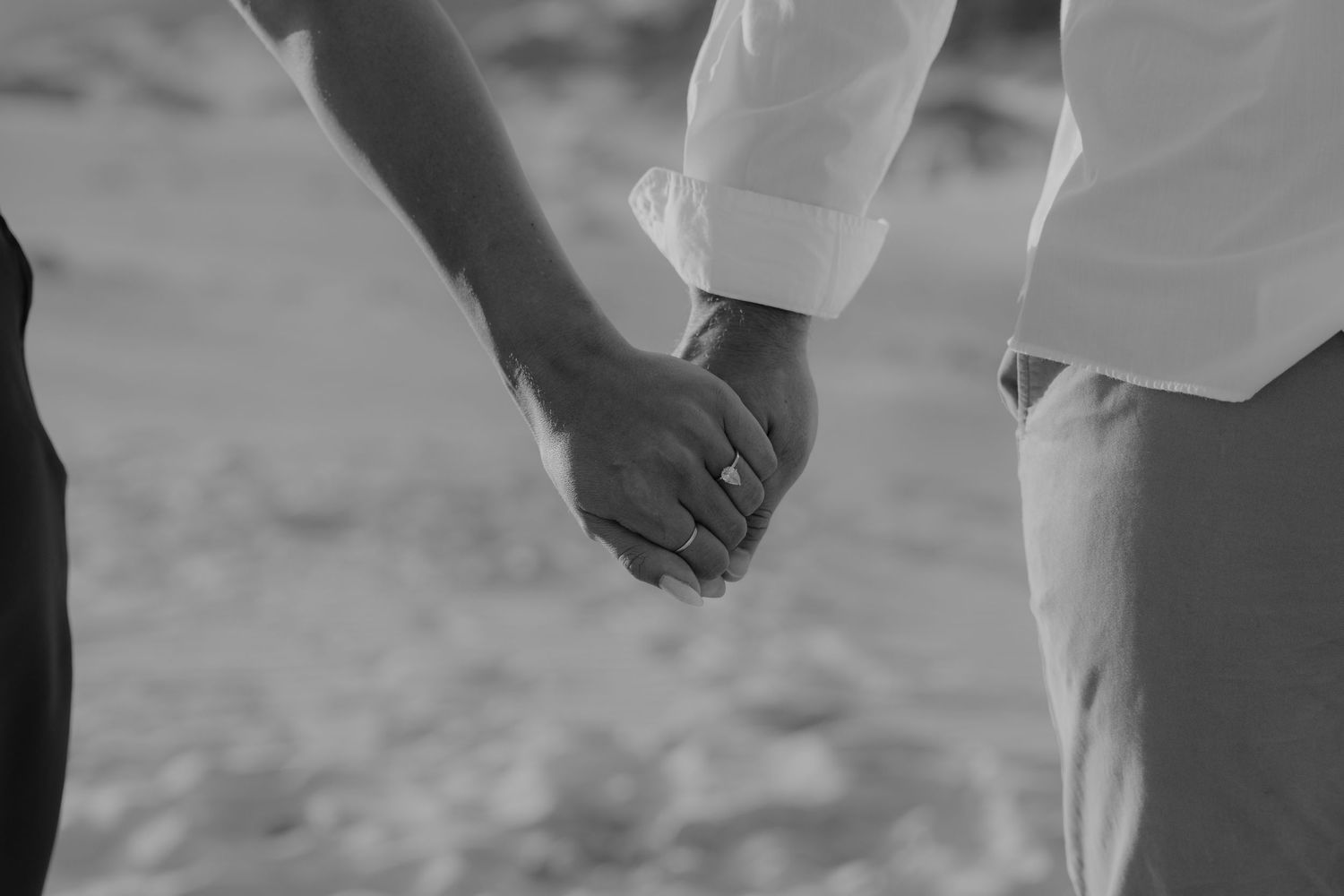 Black and white photo of a couple holding hands, with a ring visible, symbolizing love and commitment.