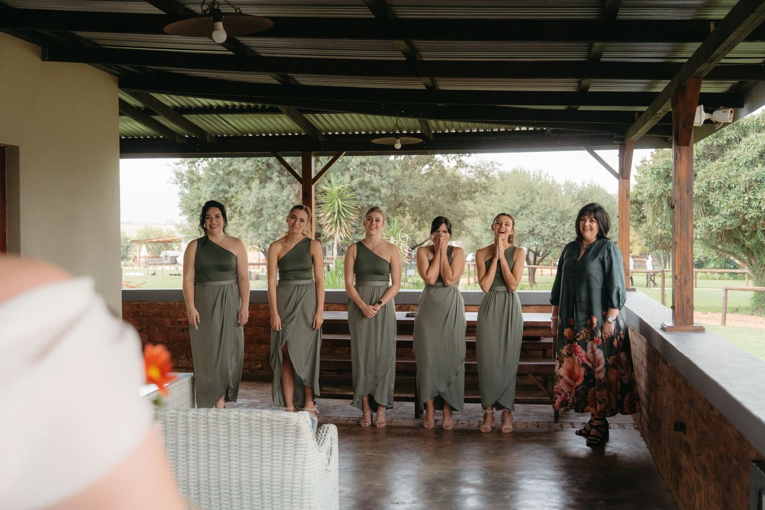 Group in matching sage green dresses standing together on a covered porch.