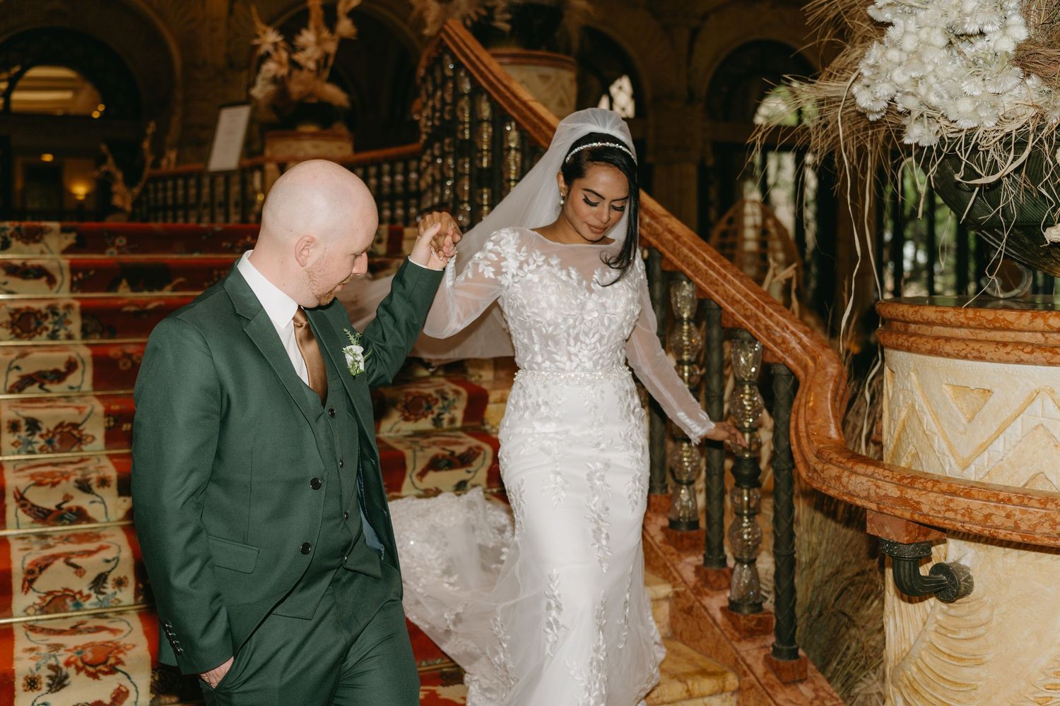 A couple enjoys a candid moment on an ornate staircase during their wedding celebration.