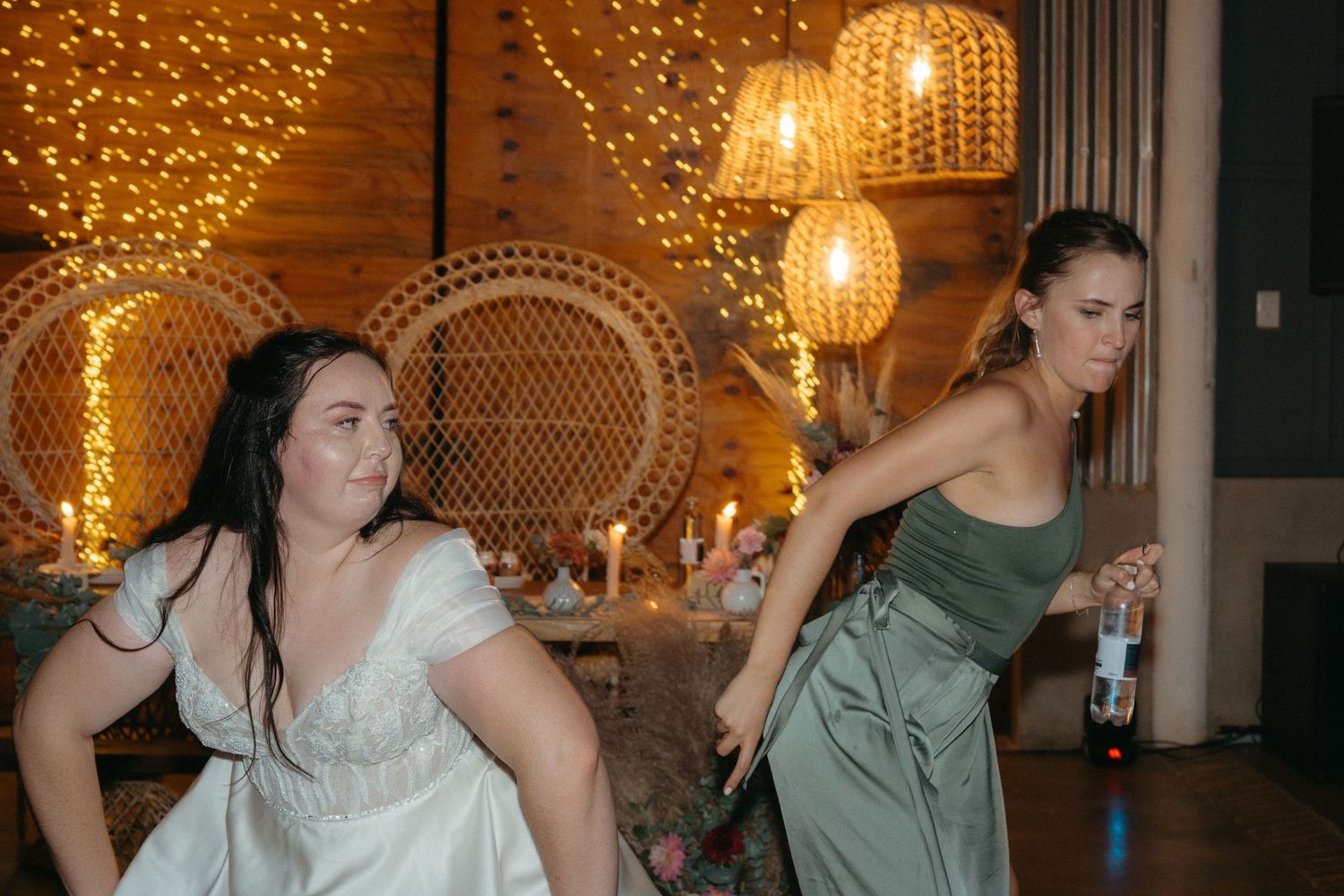 Wedding guests dancing under warm golden string lights and rattan pendant lamps.