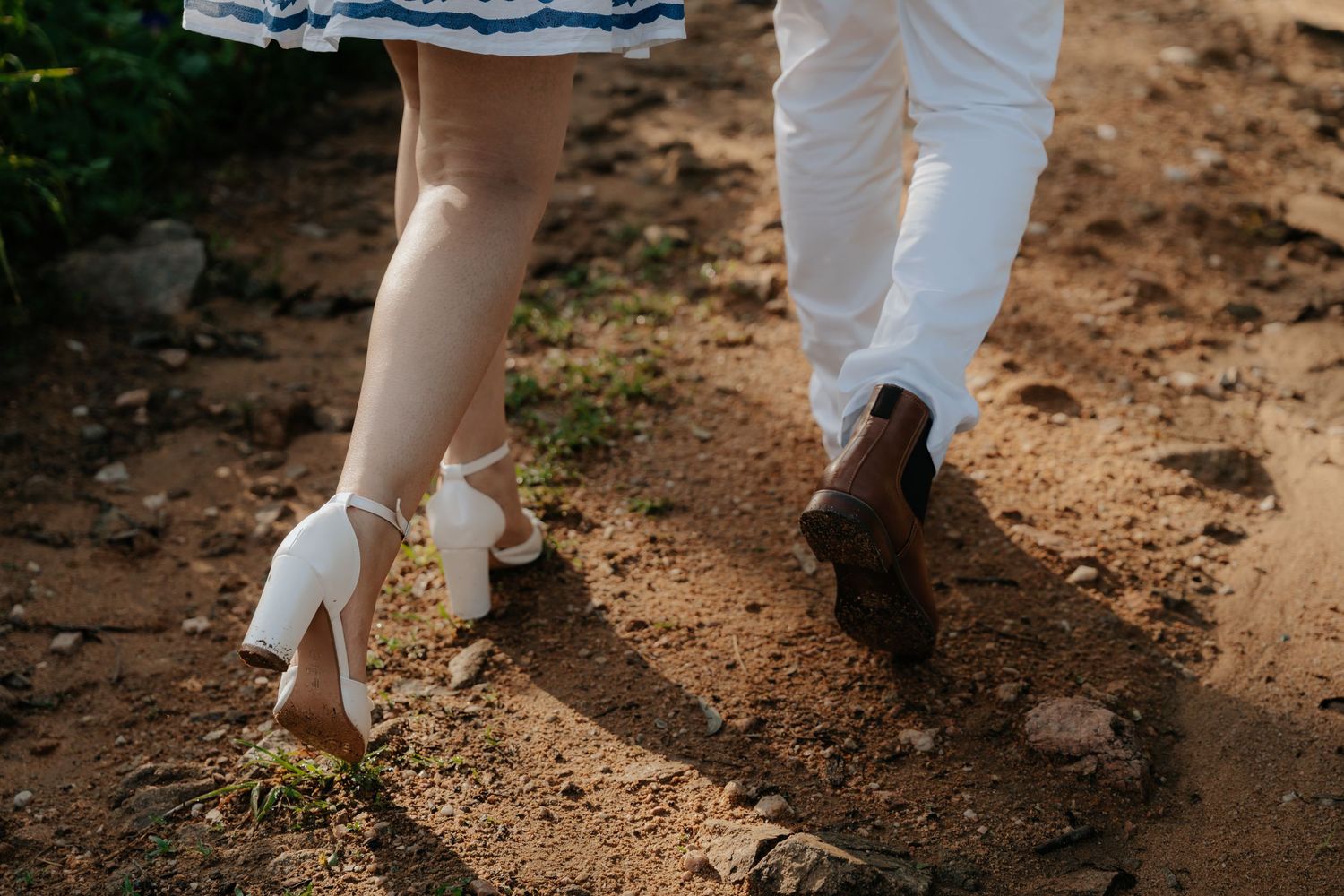 Cropped view of feet and legs dancing on a rustic dirt path surrounded by greenery.