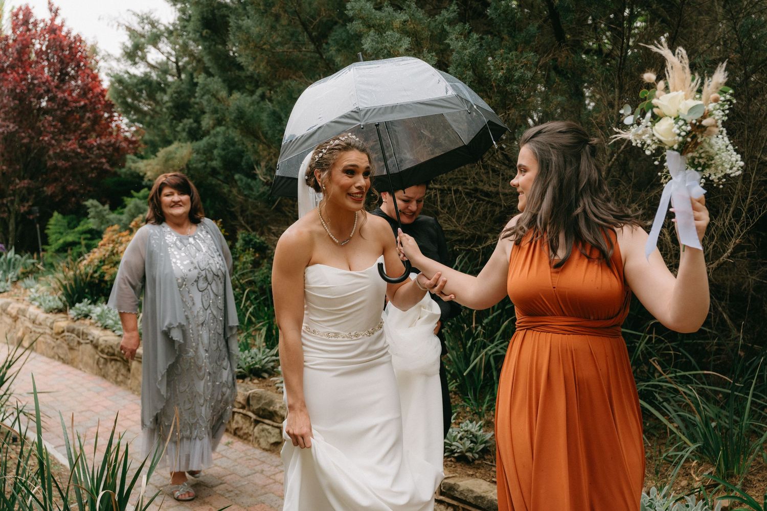 Wedding party members in white and rust-colored dresses pose together outdoors.