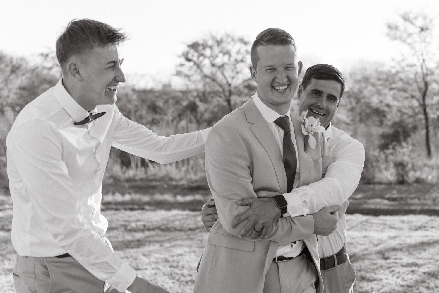Groomsmen in white shirts share laughs during outdoor wedding photo session.