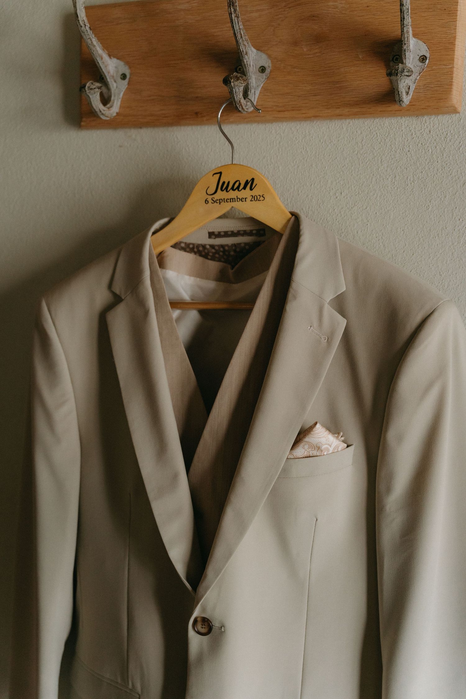 Beige suit jackets hanging neatly on wooden coat hooks against a white wall.