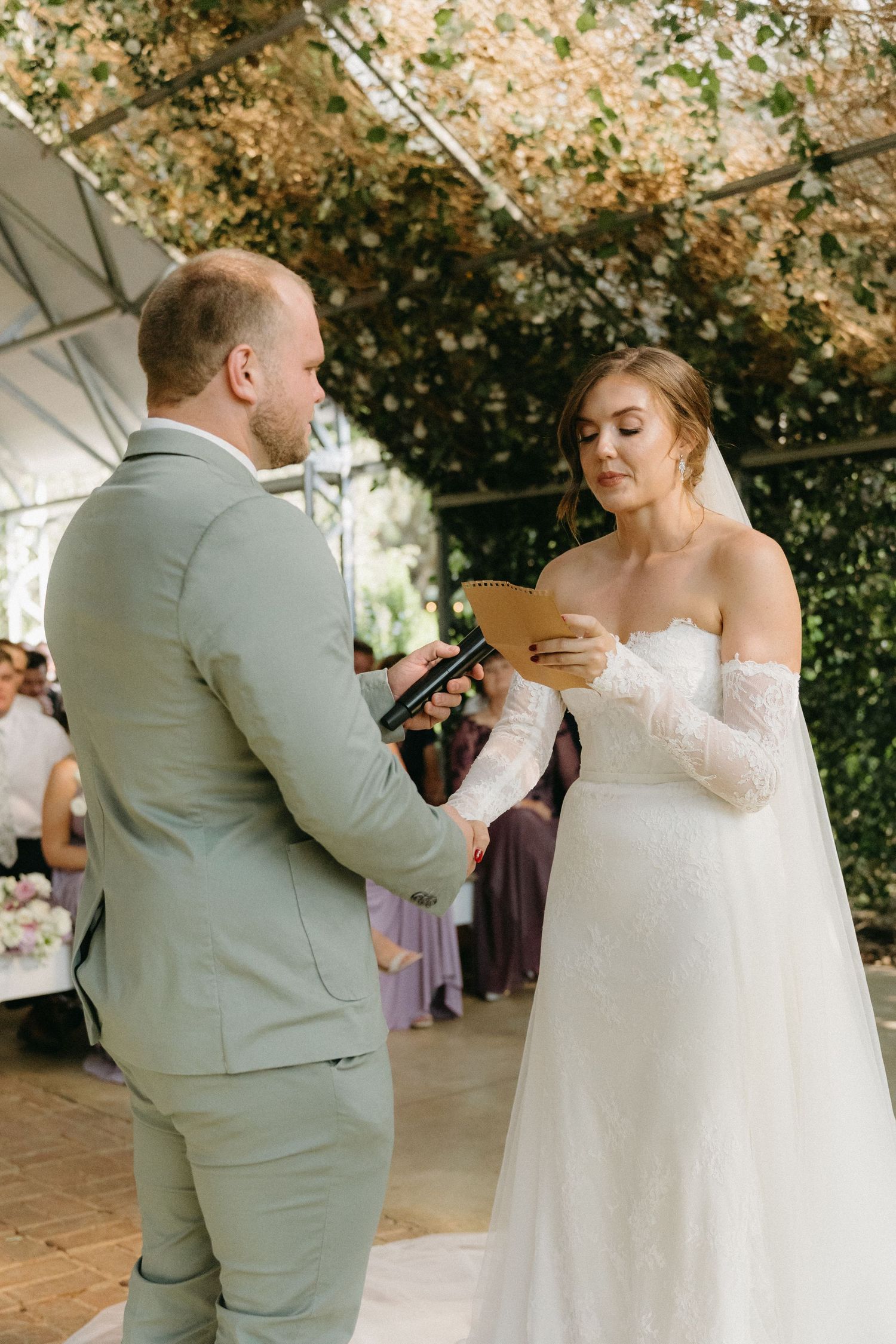 Couple exchanging wedding vows under a floral-adorned canopy during an outdoor ceremony.