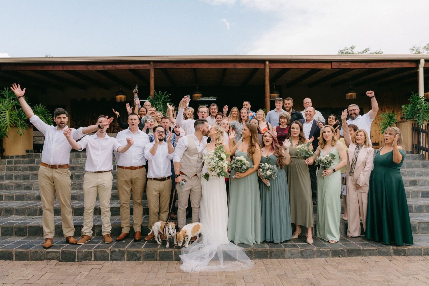 Large wedding party poses together outdoors in coordinated formal attire.