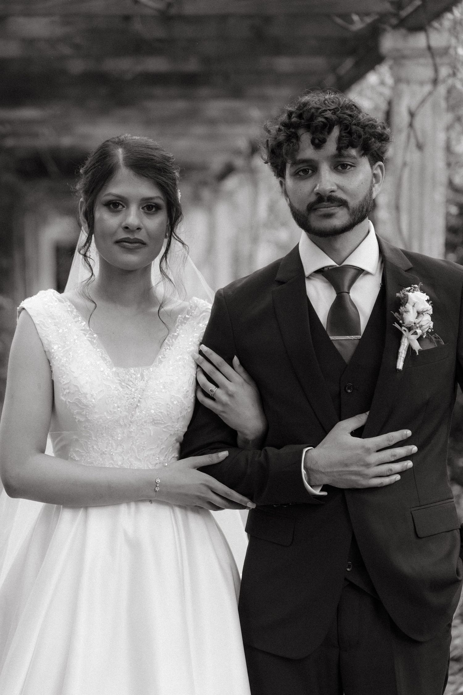 A black and white wedding portrait of a couple in formal attire under a covered walkway.