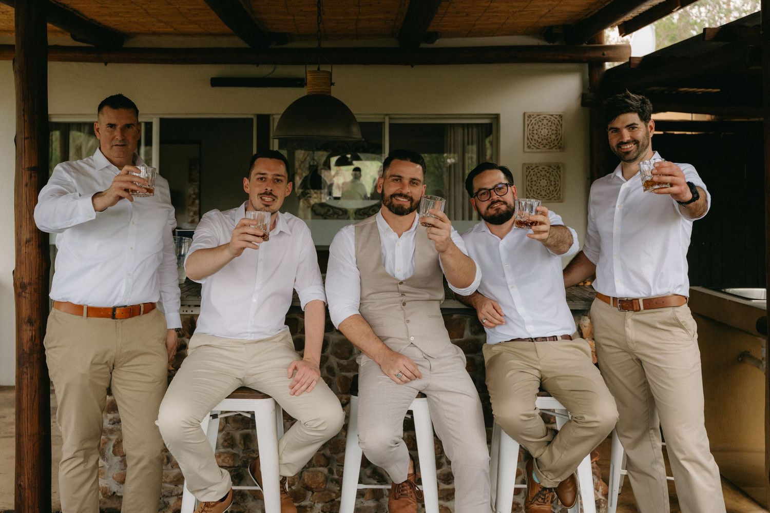 Groomsmen in white shirts and khaki pants pose together on wooden bench.