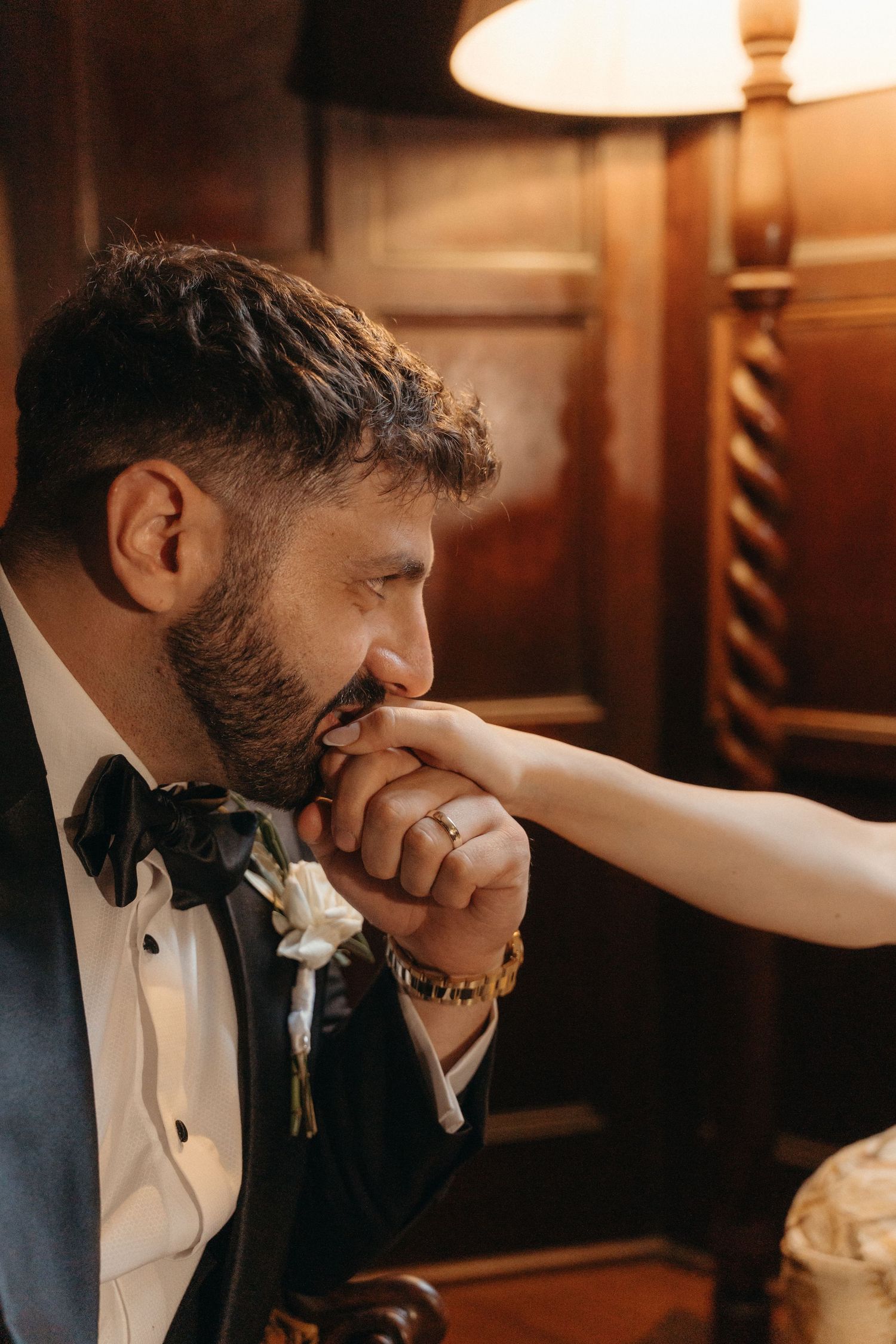 Groom in tuxedo with bow tie tenderly kissing bride's hand in warm golden light at Glenshiel in Johannesburg