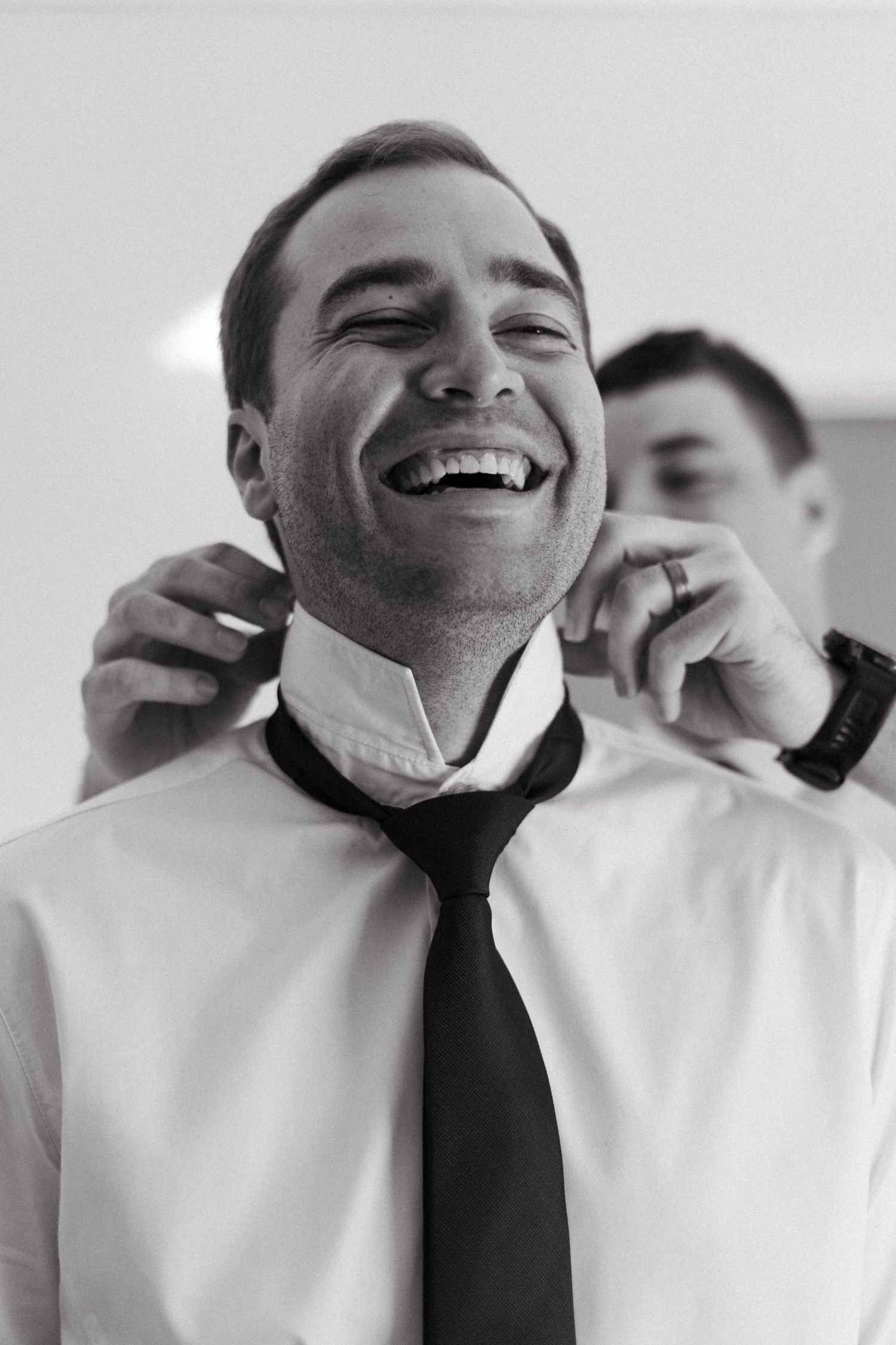 Black and white candid photo of morning wedding preparations showing adjusting of formal attire.