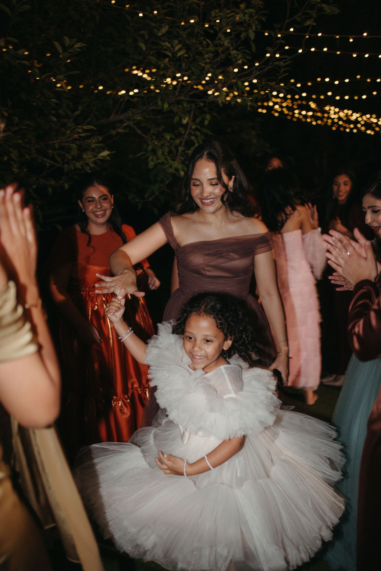 A woman in a mauve gown dances with a young girl in a white tutu dress at an outdoor wedding reception.