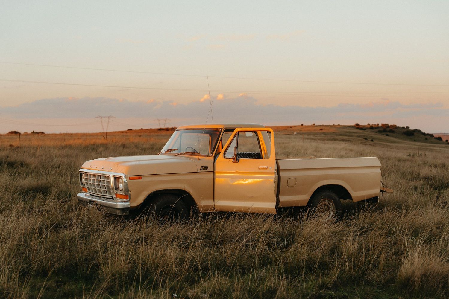 Vintage yellow Ford pickup truck parked in golden prairie grassland at sunset with dramatic sky.