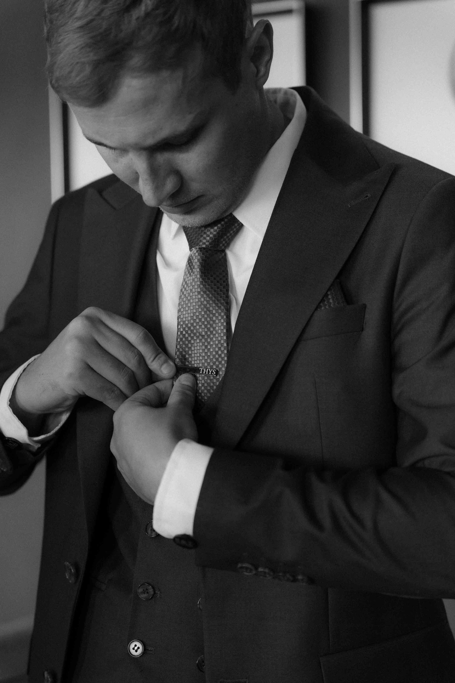 Black and white photo of a well-dressed man in a suit adjusting his cufflinks while looking down.