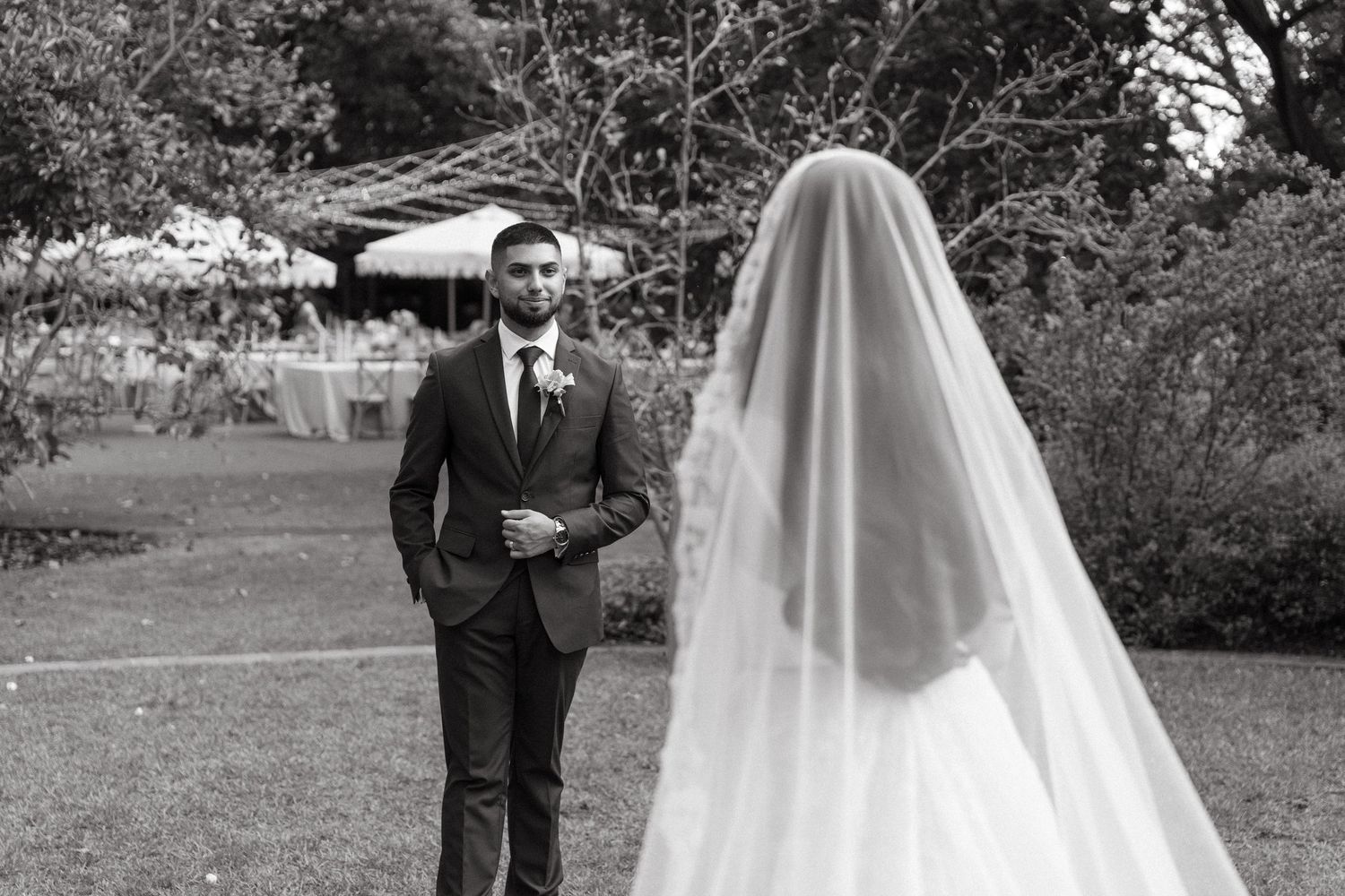 Black and white photo of a groom seeing his bride in a wedding veil for the first time outdoors.