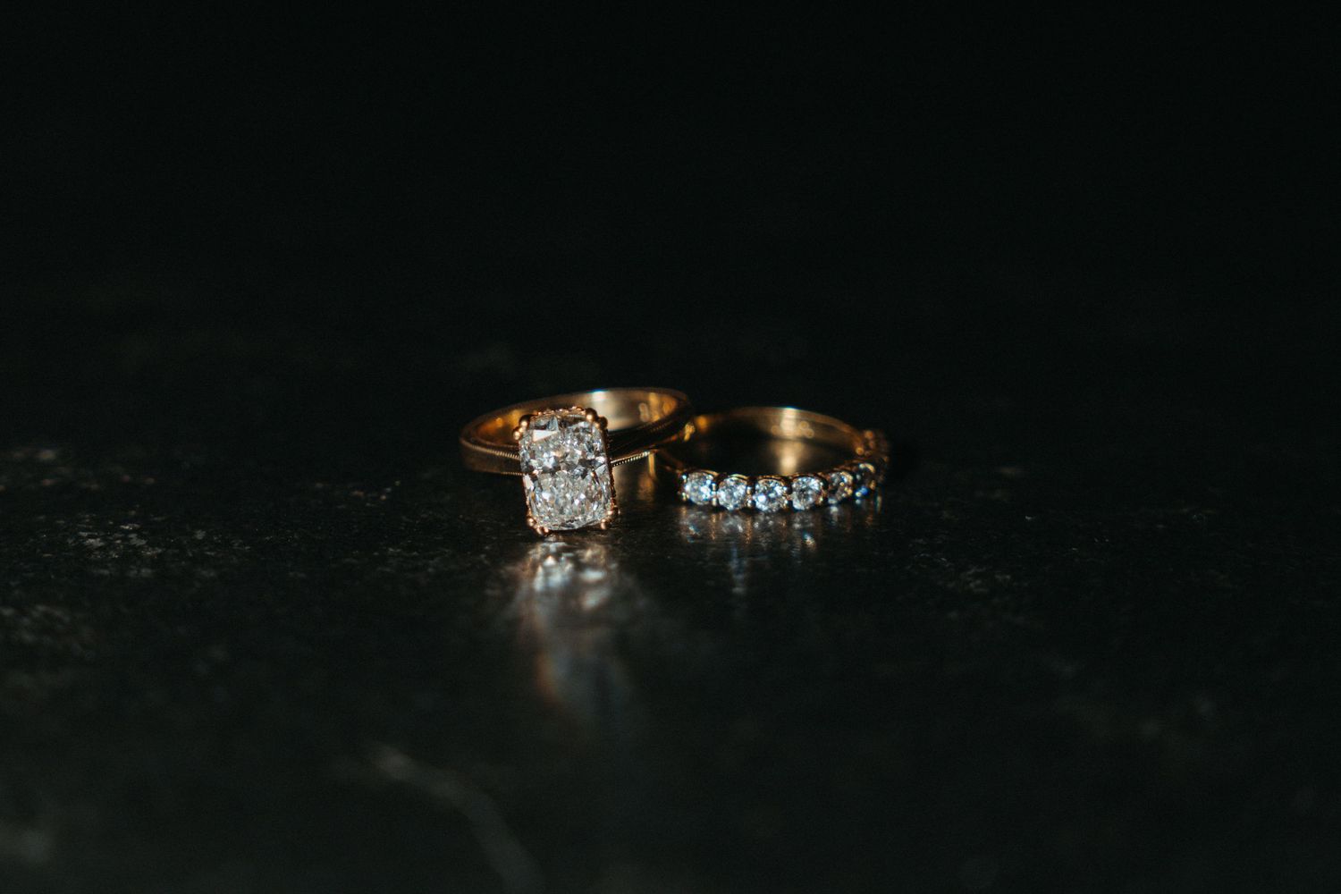 Two gold diamond rings, an engagement ring and wedding band, displayed on a dark reflective surface.