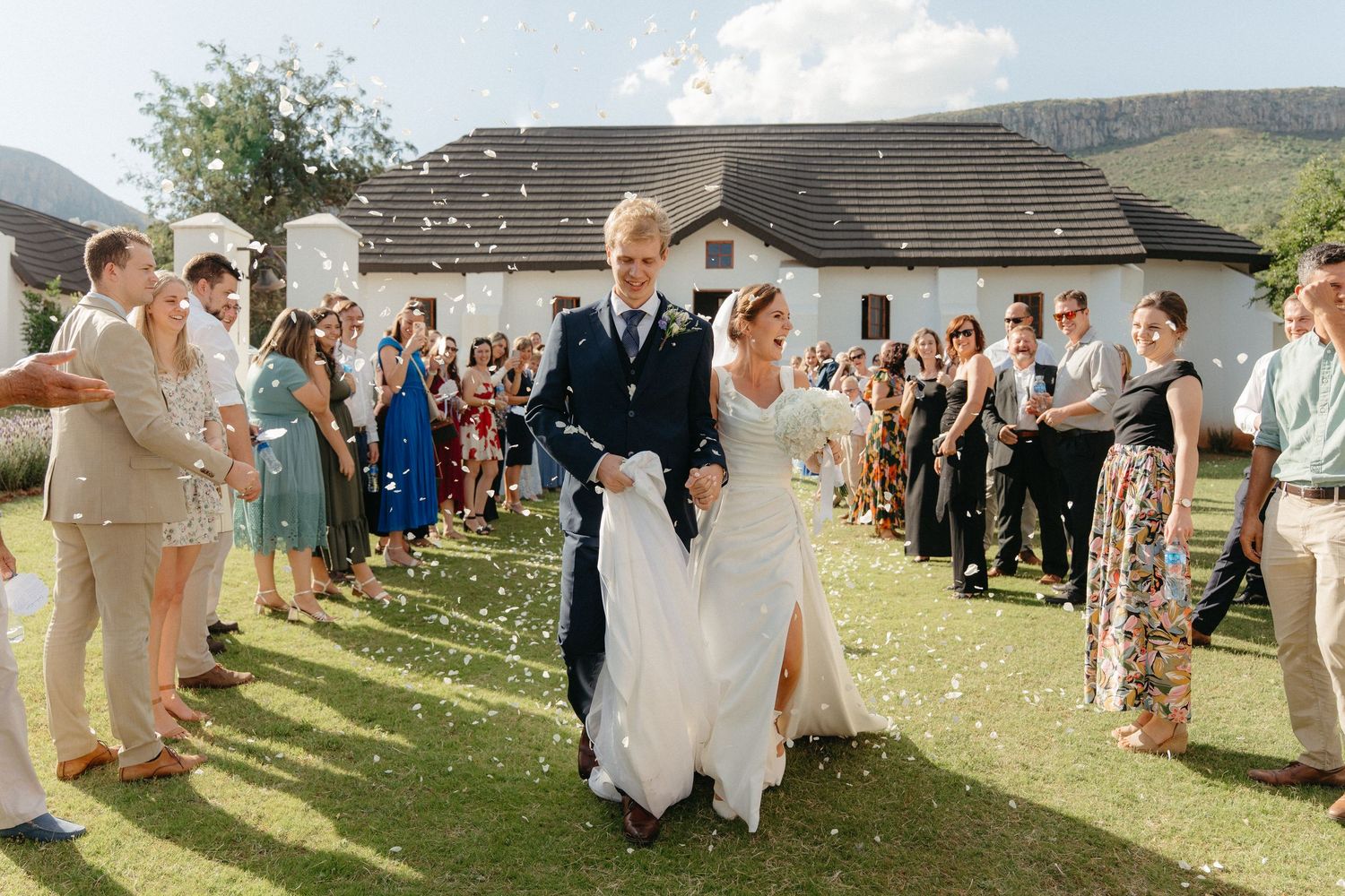 Bride and groom walk through confetti shower surrounded by cheering guests at Steynshoop Valley Lodge