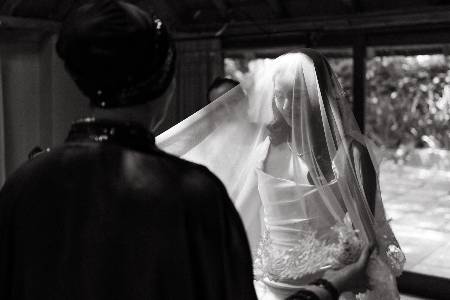 Black and white wedding photograph showing bride in veil with delicate dress details.