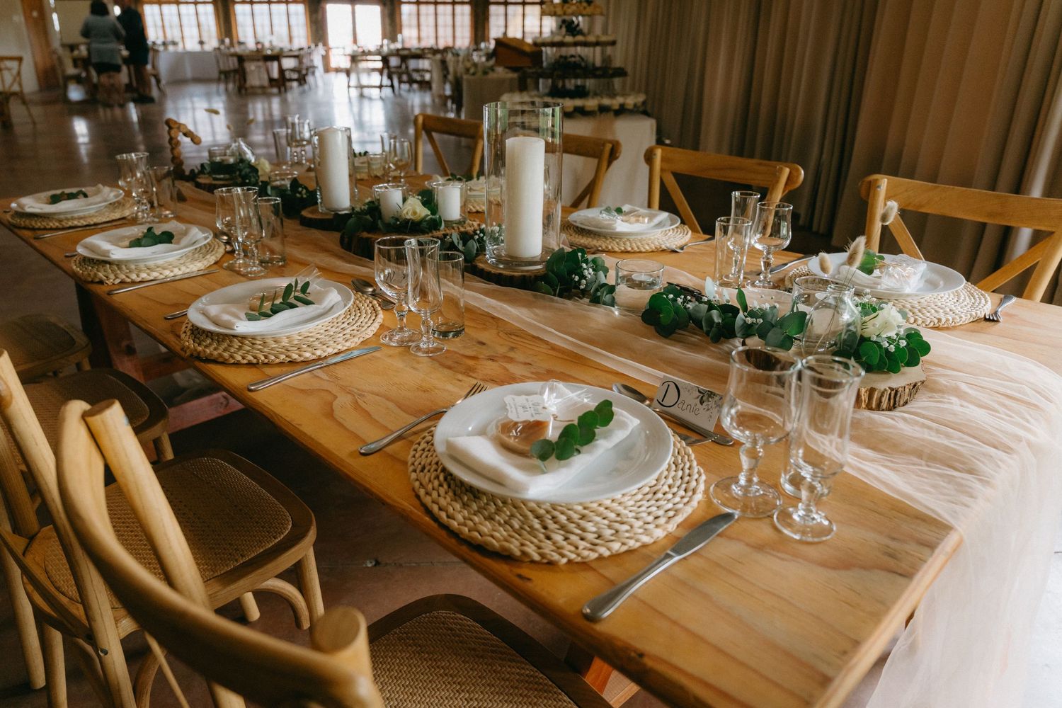 Elegant rustic wedding reception table setting with wooden chairs and woven placemats.
