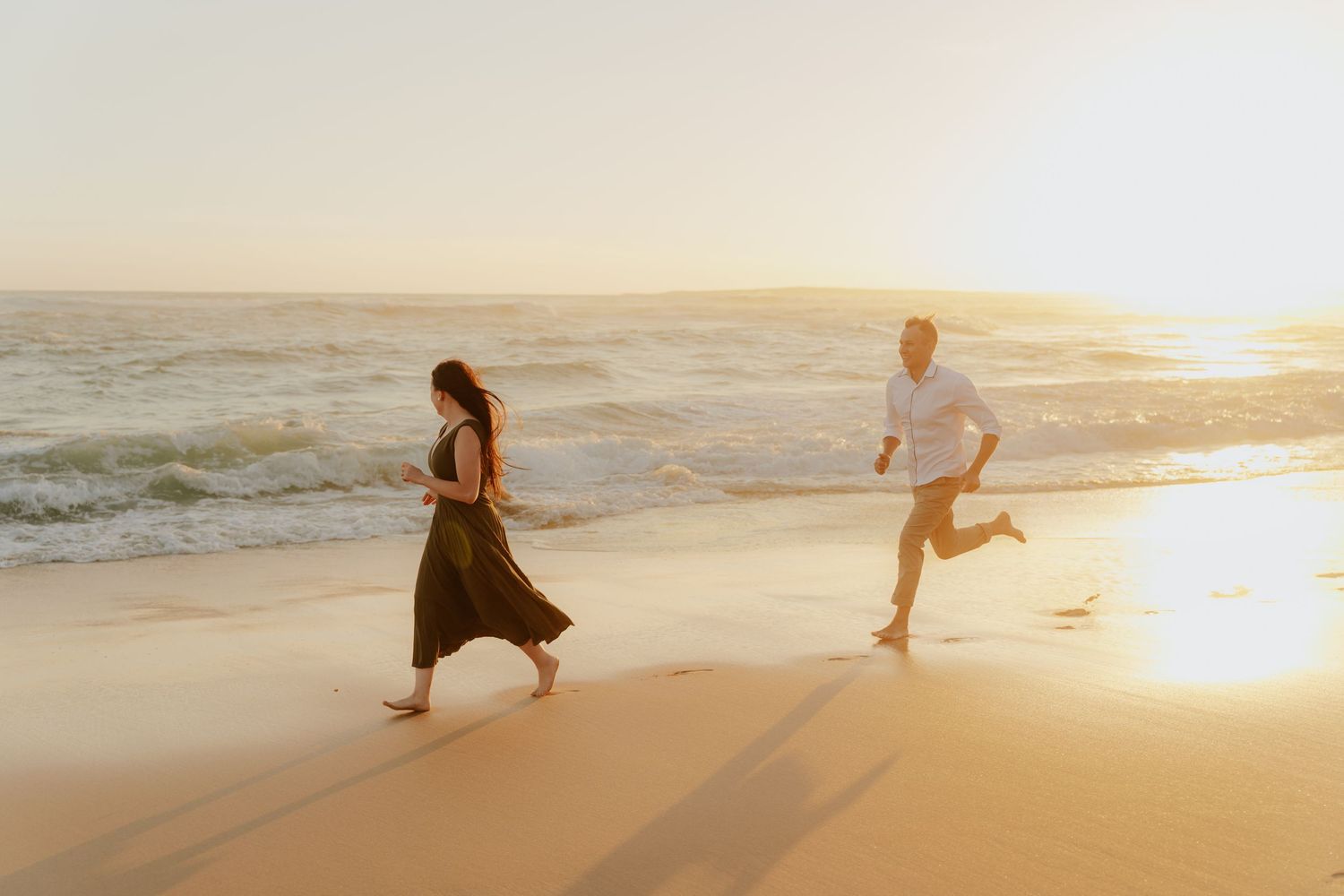 People practicing yoga poses on a sandy beach at sunset with golden light reflecting off the ocean waves.