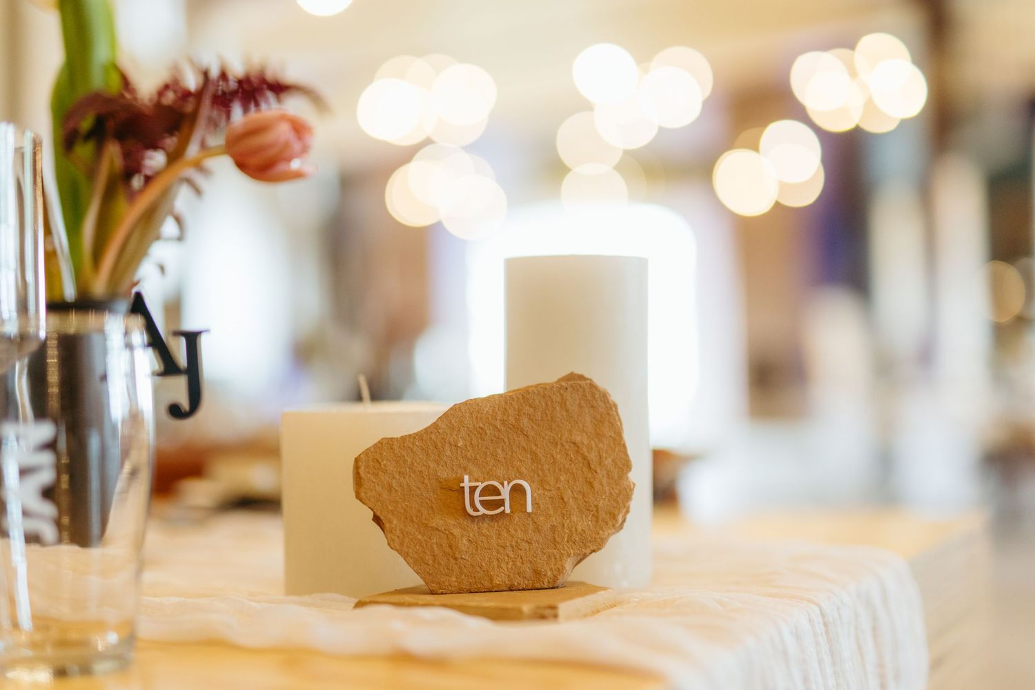 Wedding table detail with a golden place card holder and soft bokeh lights in the background.