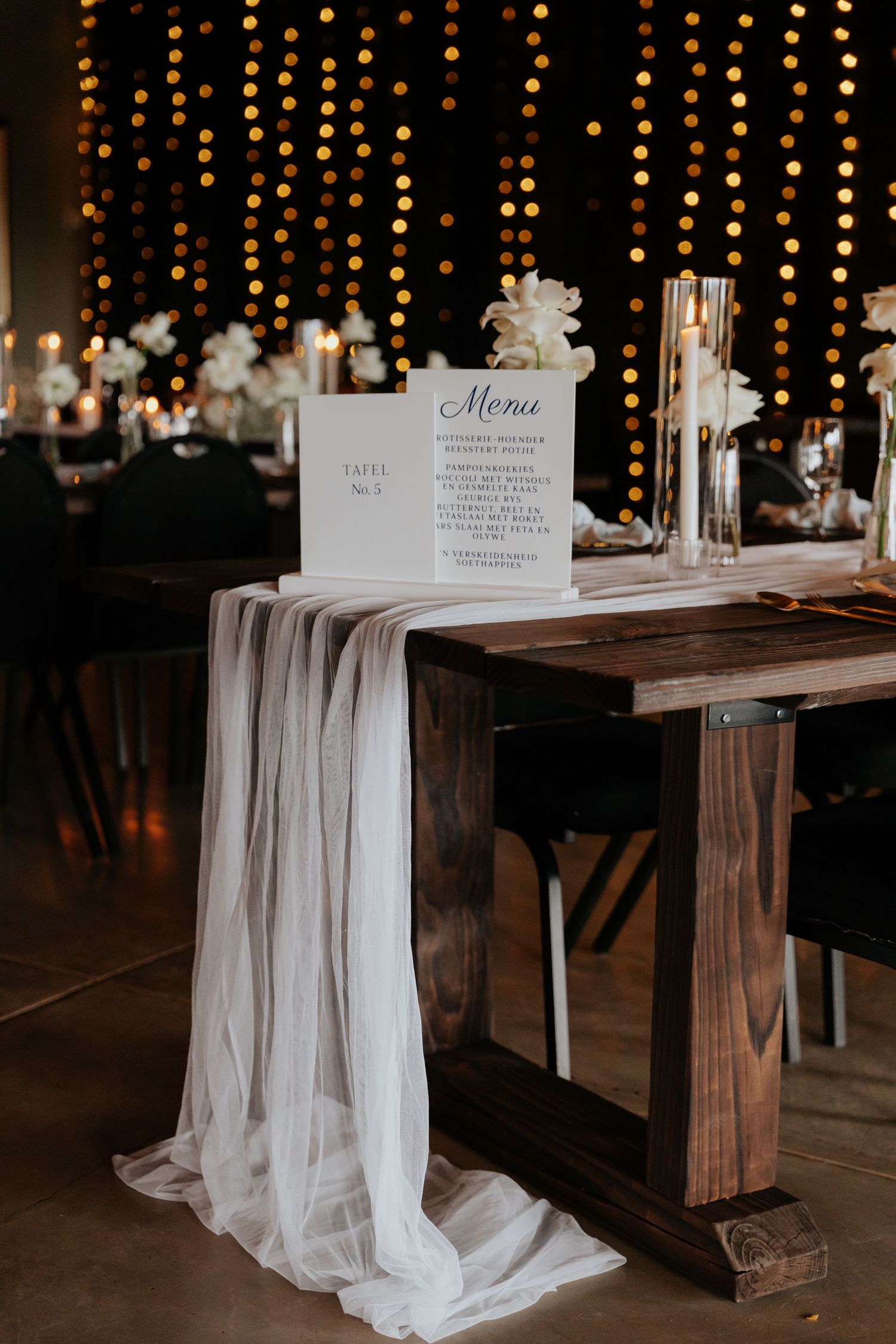 Rustic wedding reception tables with white draping and string lights create romantic ambiance.
