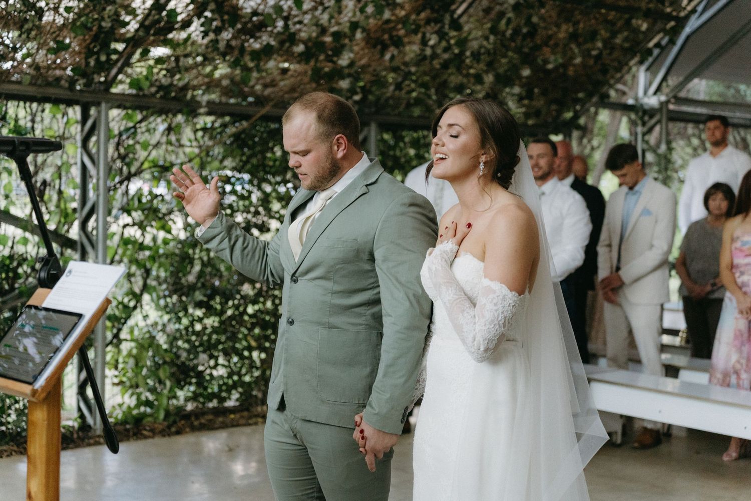 A couple in wedding attire joyfully celebrate during their ceremony in a lush garden setting.