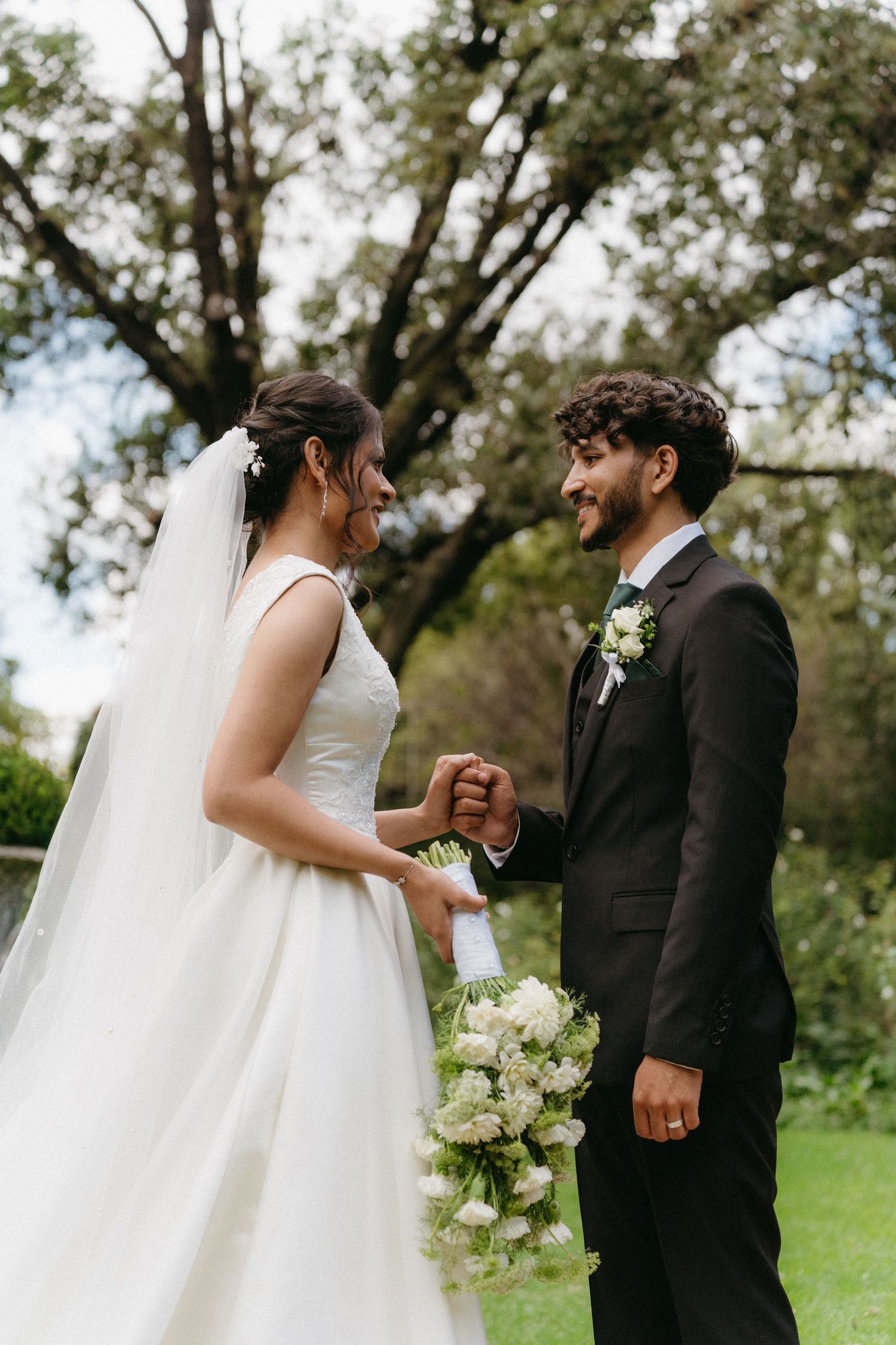 Newlyweds share a joyful moment together in a garden setting while holding hands and white bouquet.