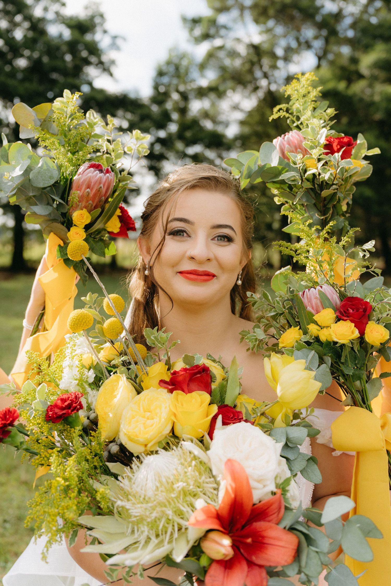 Vibrant bridal bouquet featuring yellow, red, and white flowers with eucalyptus accents in a garden setting.