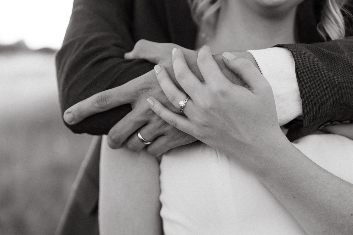 Close-up black and white photo of wedding rings and hands embracing.