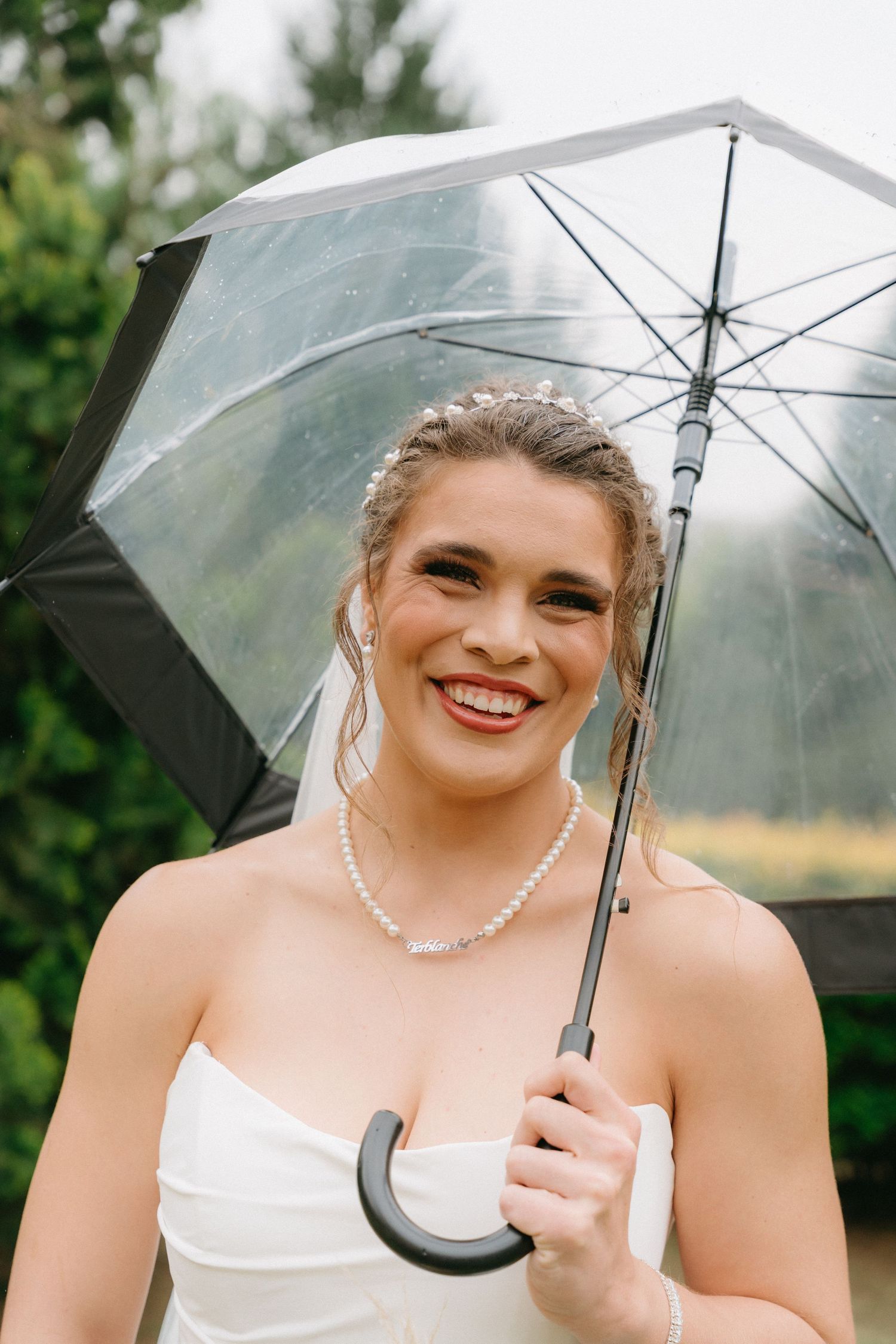 Bride holding clear umbrella poses with joyful expression in outdoor wedding photos.