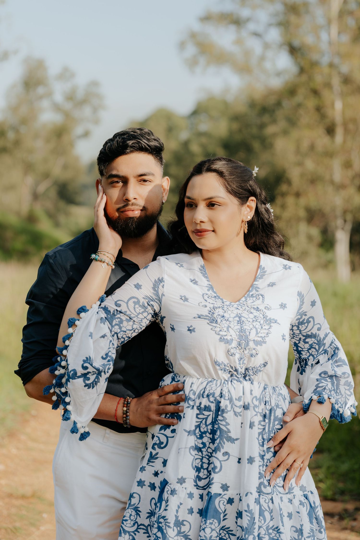 A romantic couple poses together on a nature trail wearing matching blue and white outfits.