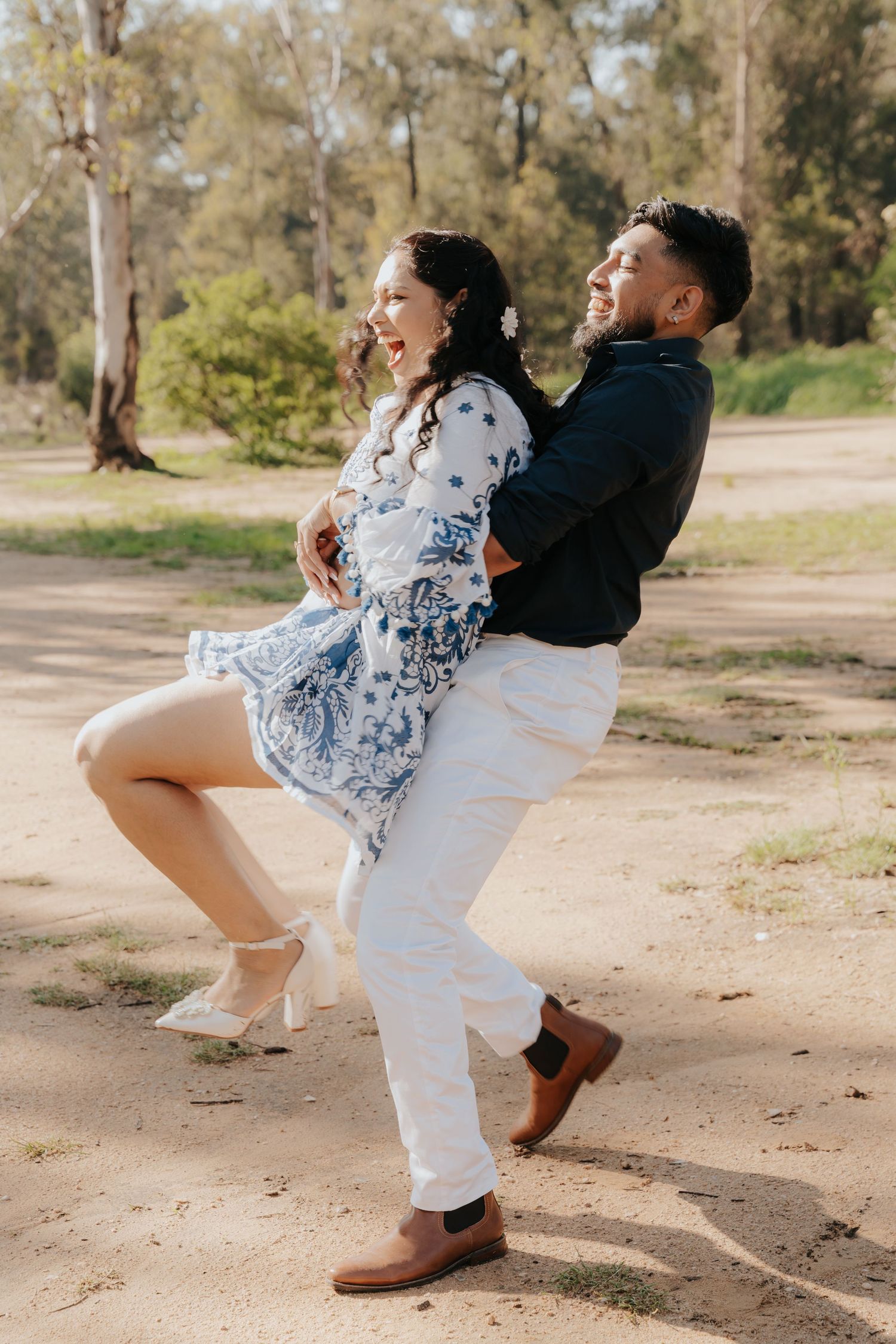 A playful couple performs fun dance moves together on a dirt path surrounded by trees.