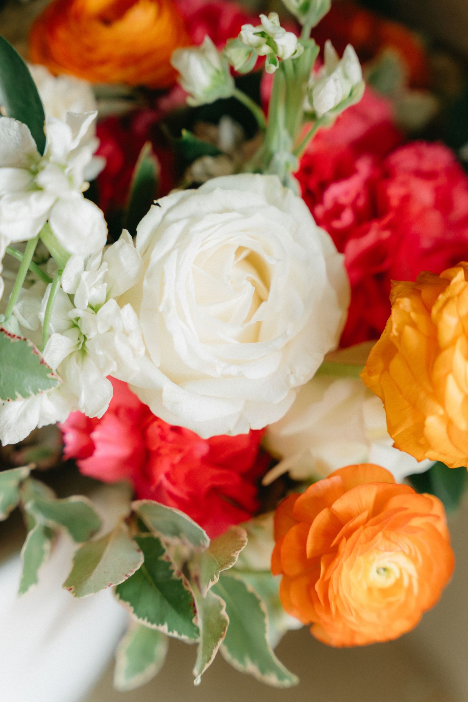 Close-up of a romantic wedding bouquet featuring white roses, orange ranunculus, and red flowers.