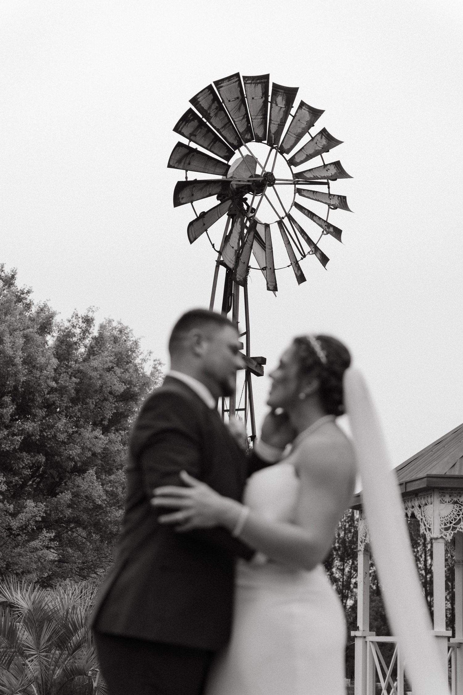 Black and white wedding photos show a romantic couple embracing in front of rustic windmills.