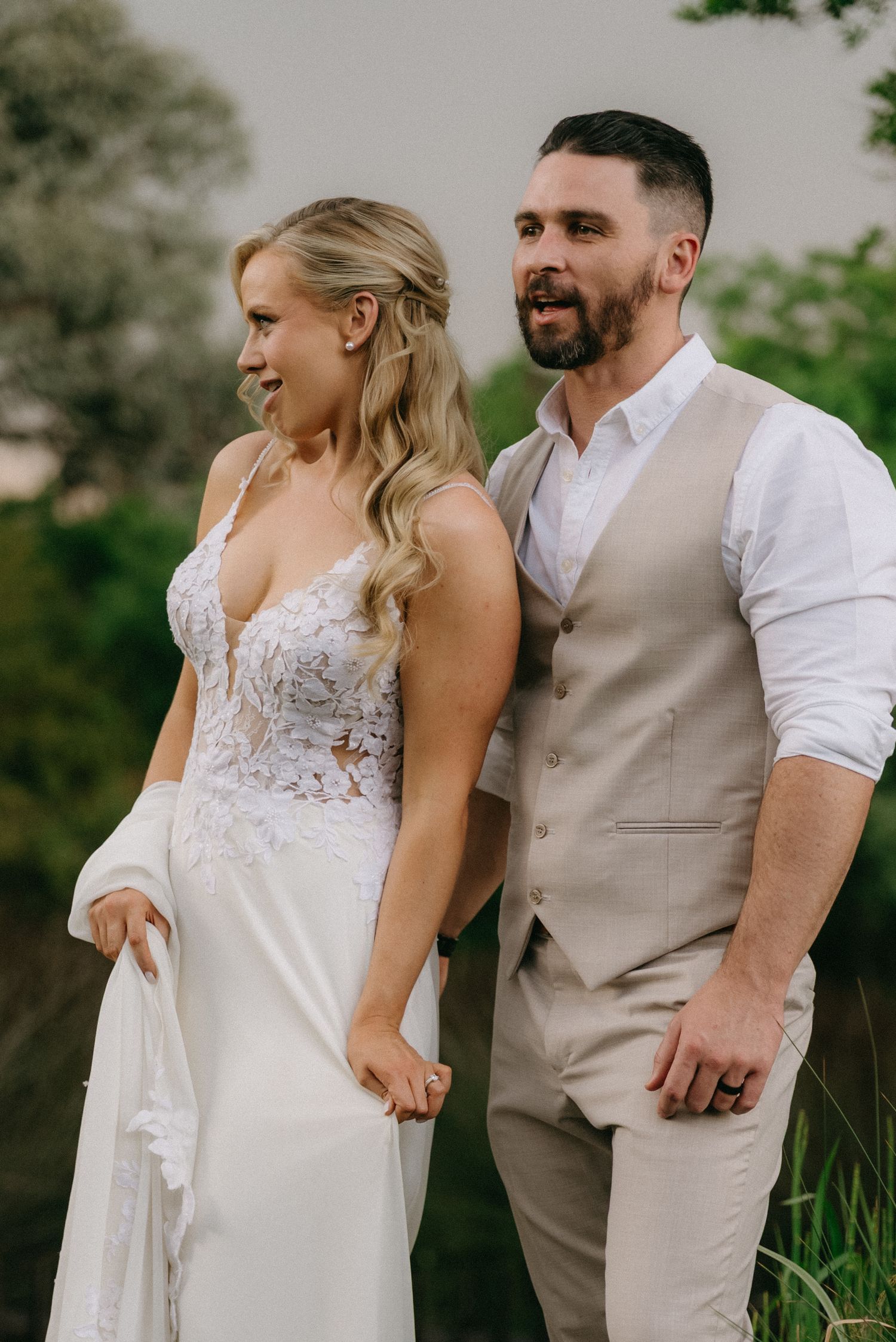 Newlyweds share intimate moment in garden setting wearing white and beige wedding attire.
