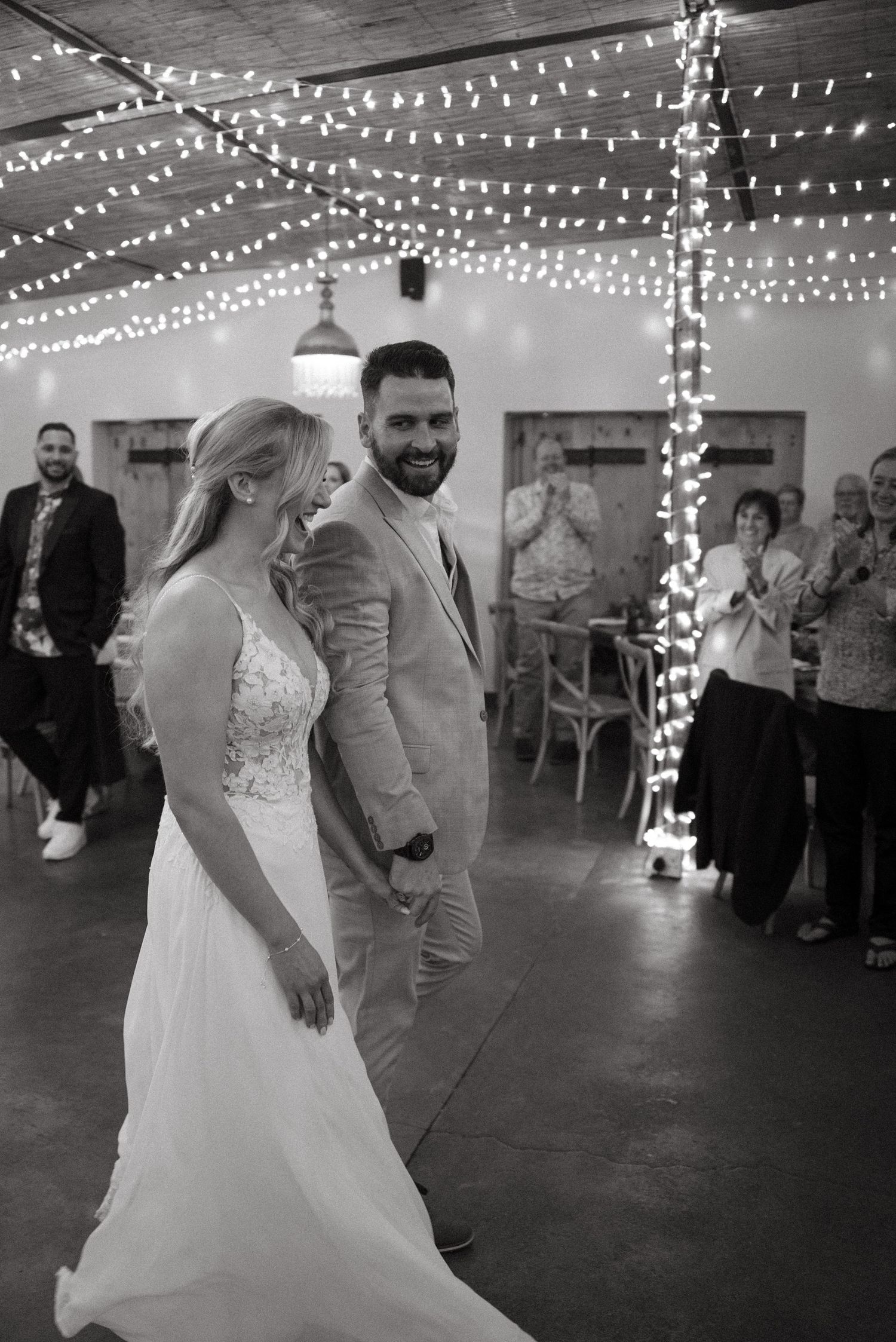 Wedding couple dances under twinkling string lights at indoor reception venue.