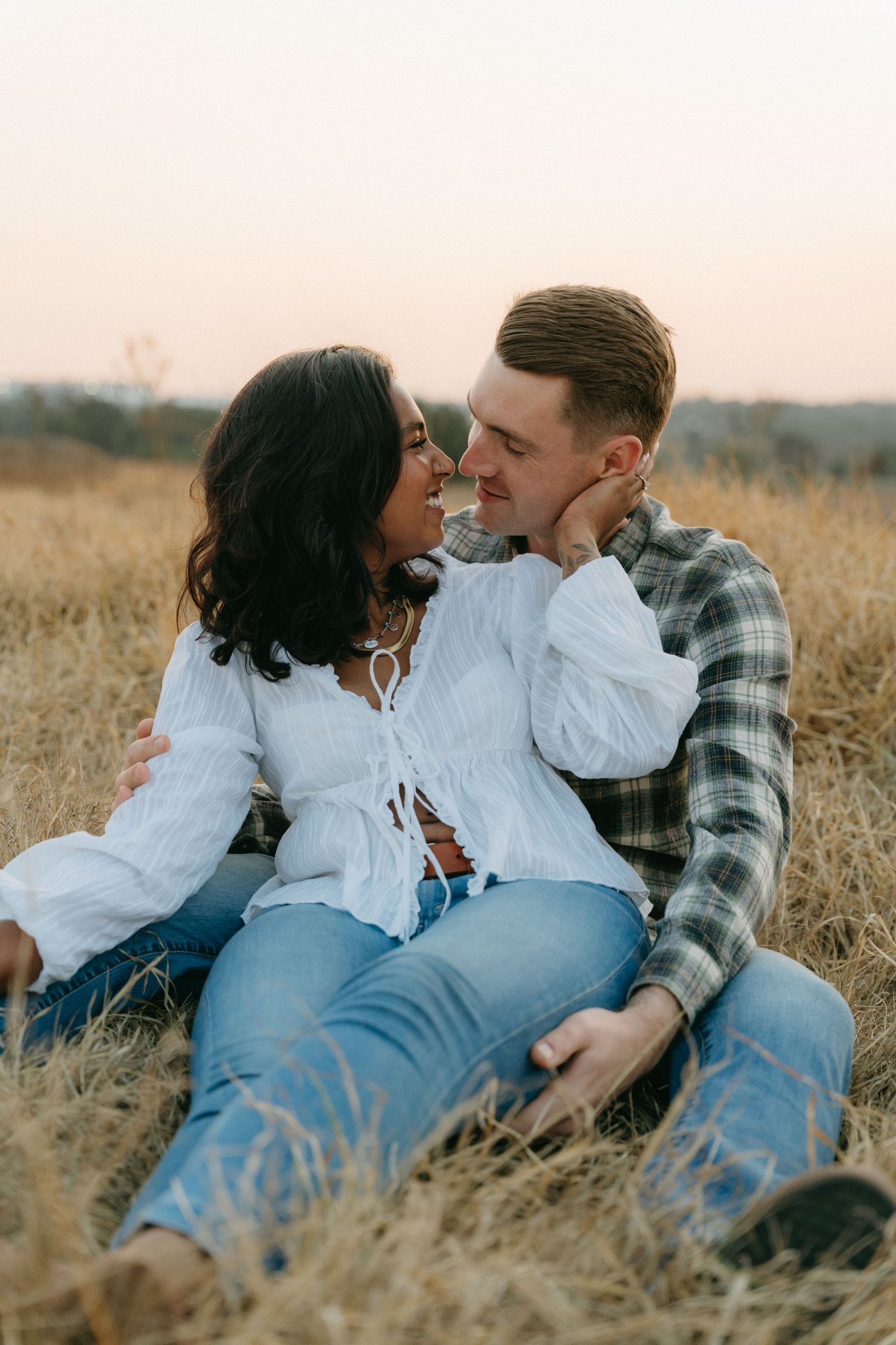 A romantic couple lounges together in a golden wheat field during a sunset photoshoot.