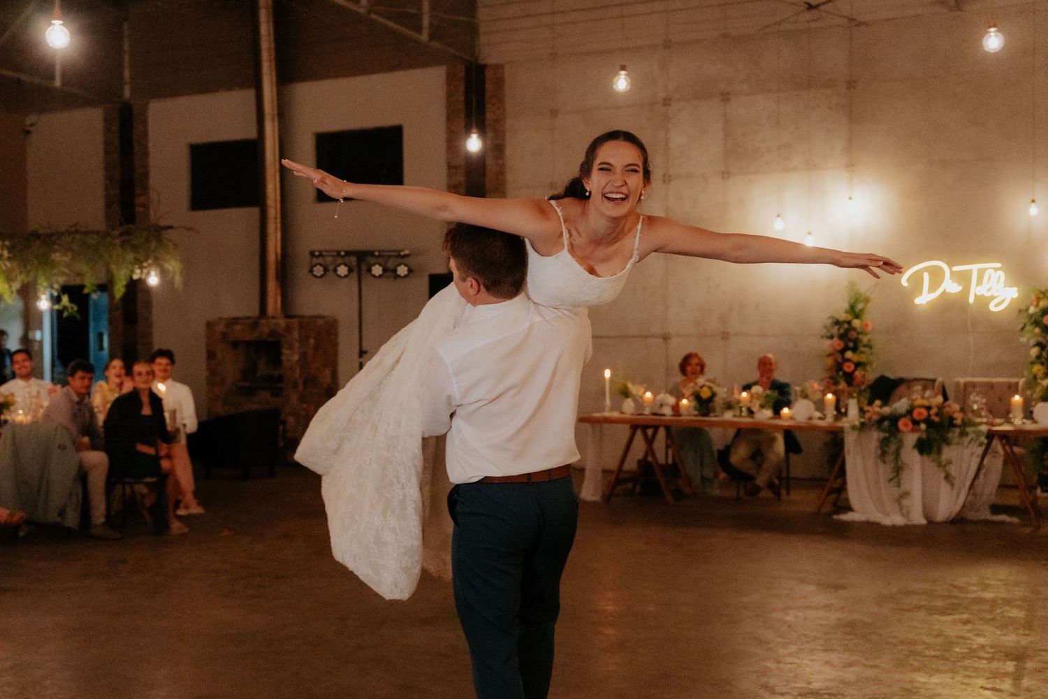 Couple performs romantic dance move during their first dance at wedding reception in industrial venue.