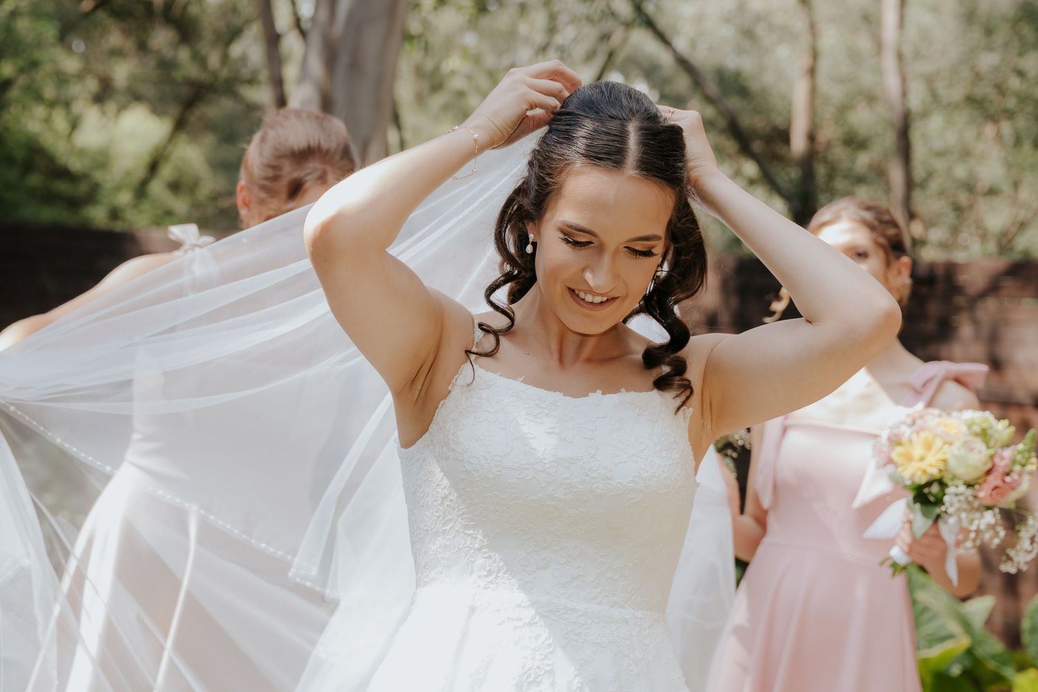 Joyful wedding party poses outdoors in pink bridesmaid dresses and white bridal gown on a sunny day.