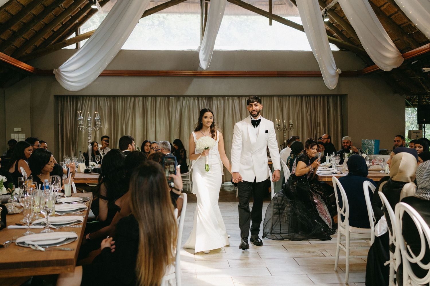 Wedding reception in a rustic venue with exposed wooden beams and elegant white draping decorations.