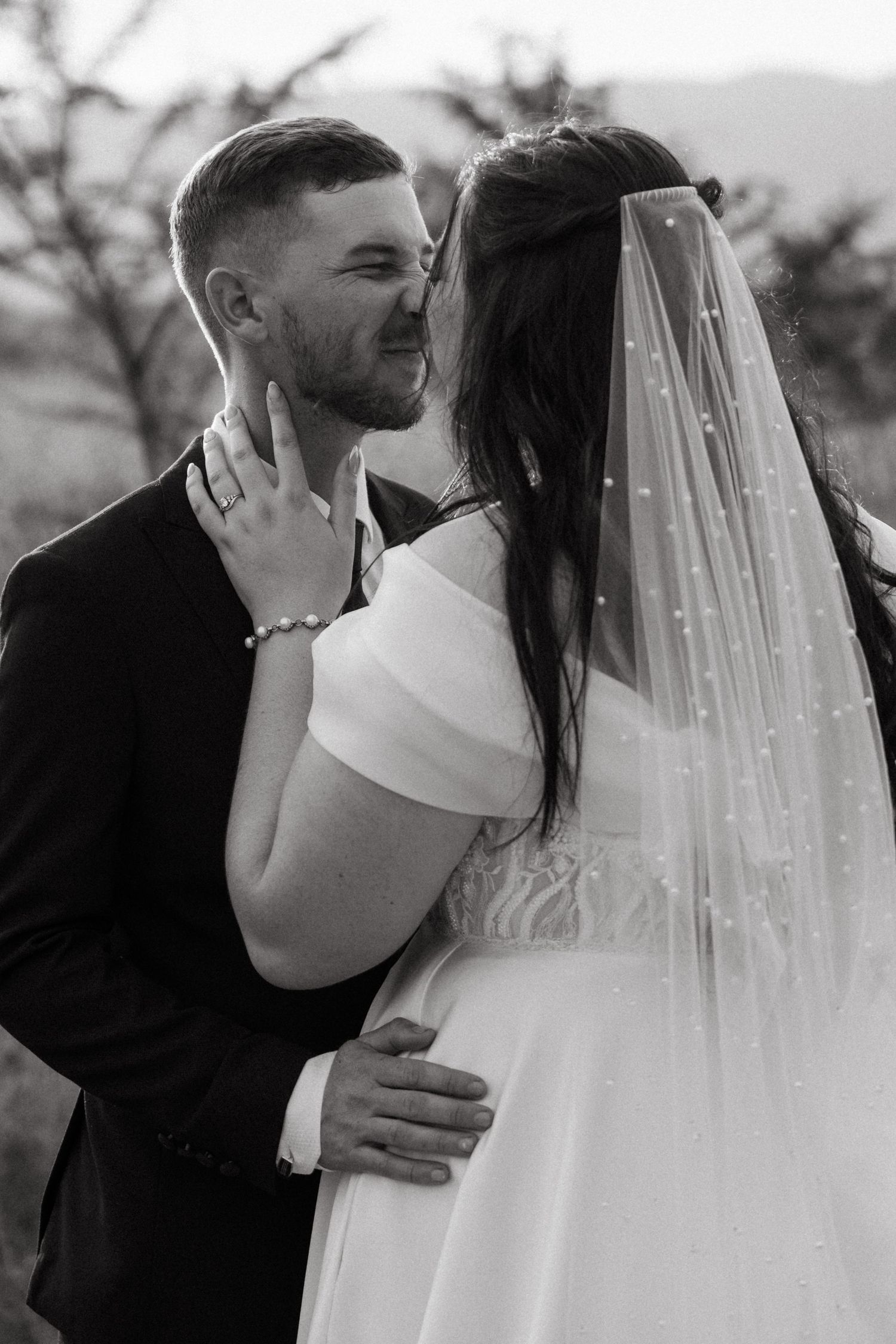 A romantic black and white portrait of newlyweds embracing during their outdoor wedding photoshoot.