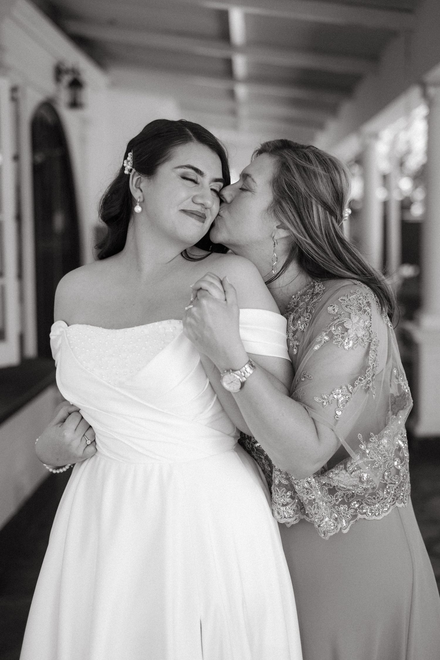 A tender black and white moment showcasing a bride in a white dress with someone wearing lace whispering to her.