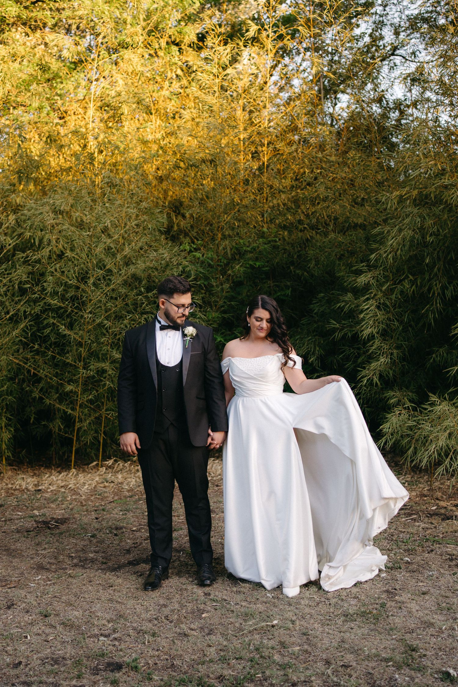 A wedding couple poses together in front of a golden bamboo grove during sunset.