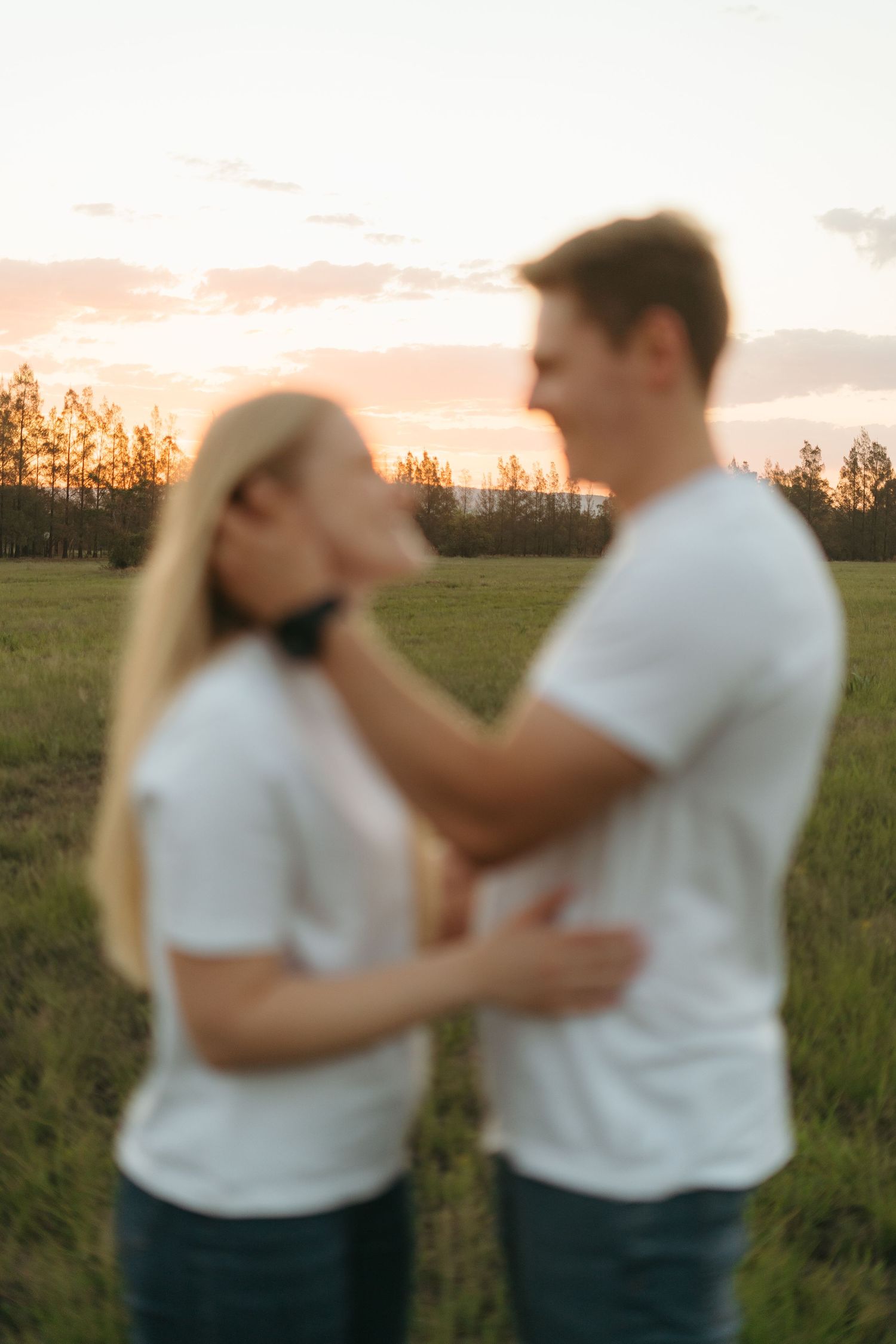 Intimate portrait of couple embracing in matching white t-shirts against sunset sky.